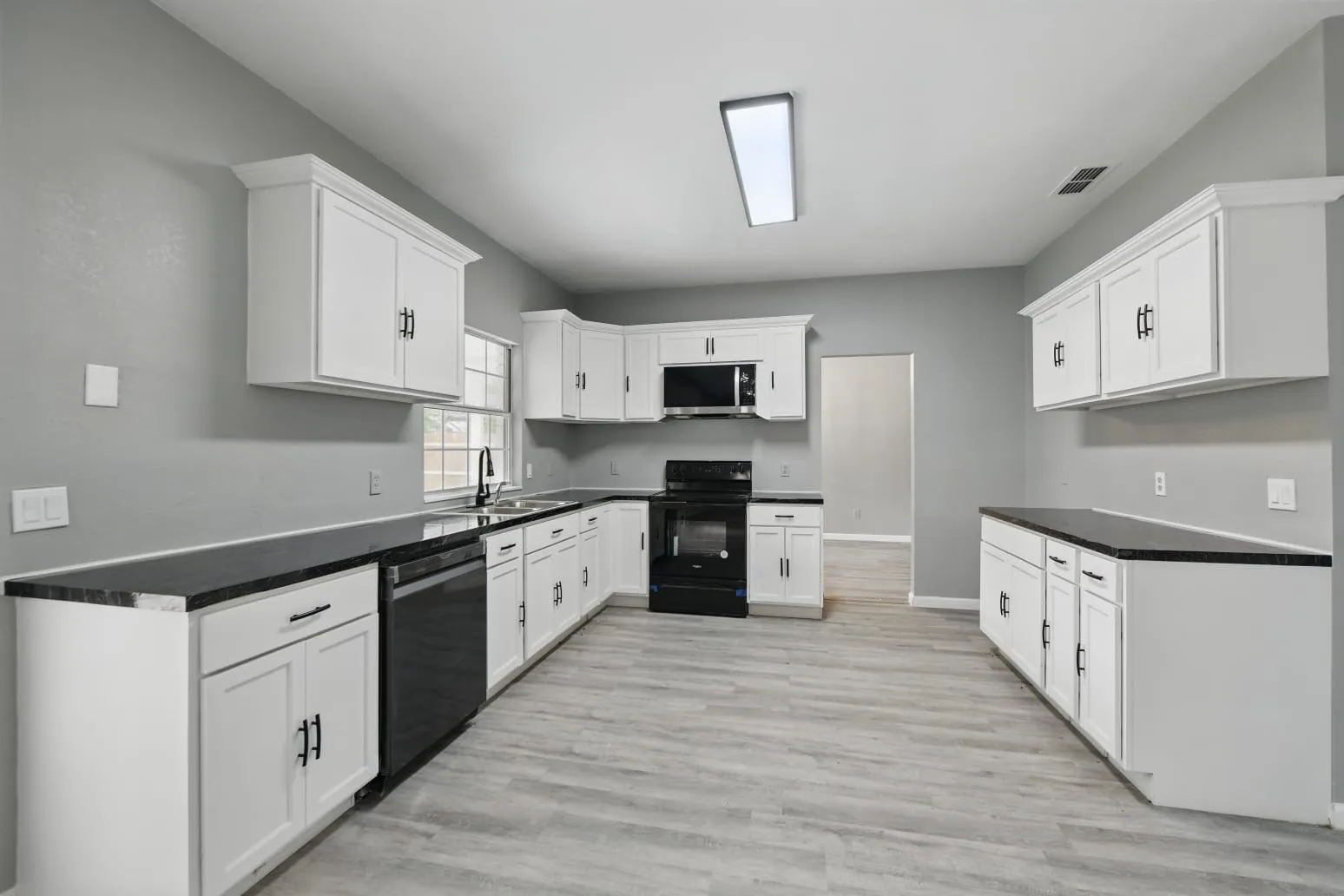 Kitchen featuring black range with electric cooktop, light wood-style floors, dishwashing machine, stainless steel microwave, and white cabinetry