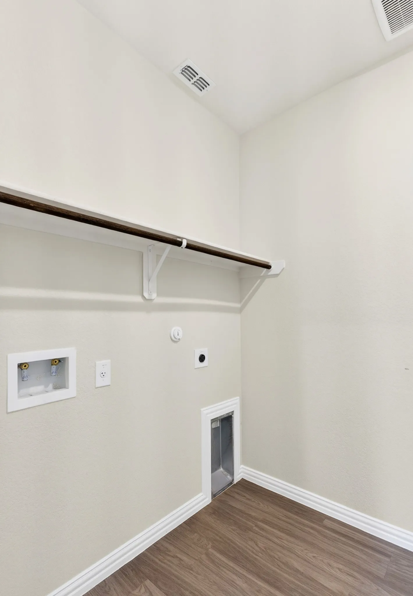 Laundry area featuring wood-finish flooring, white walls, and a convenient built-in shelf with hanging rod