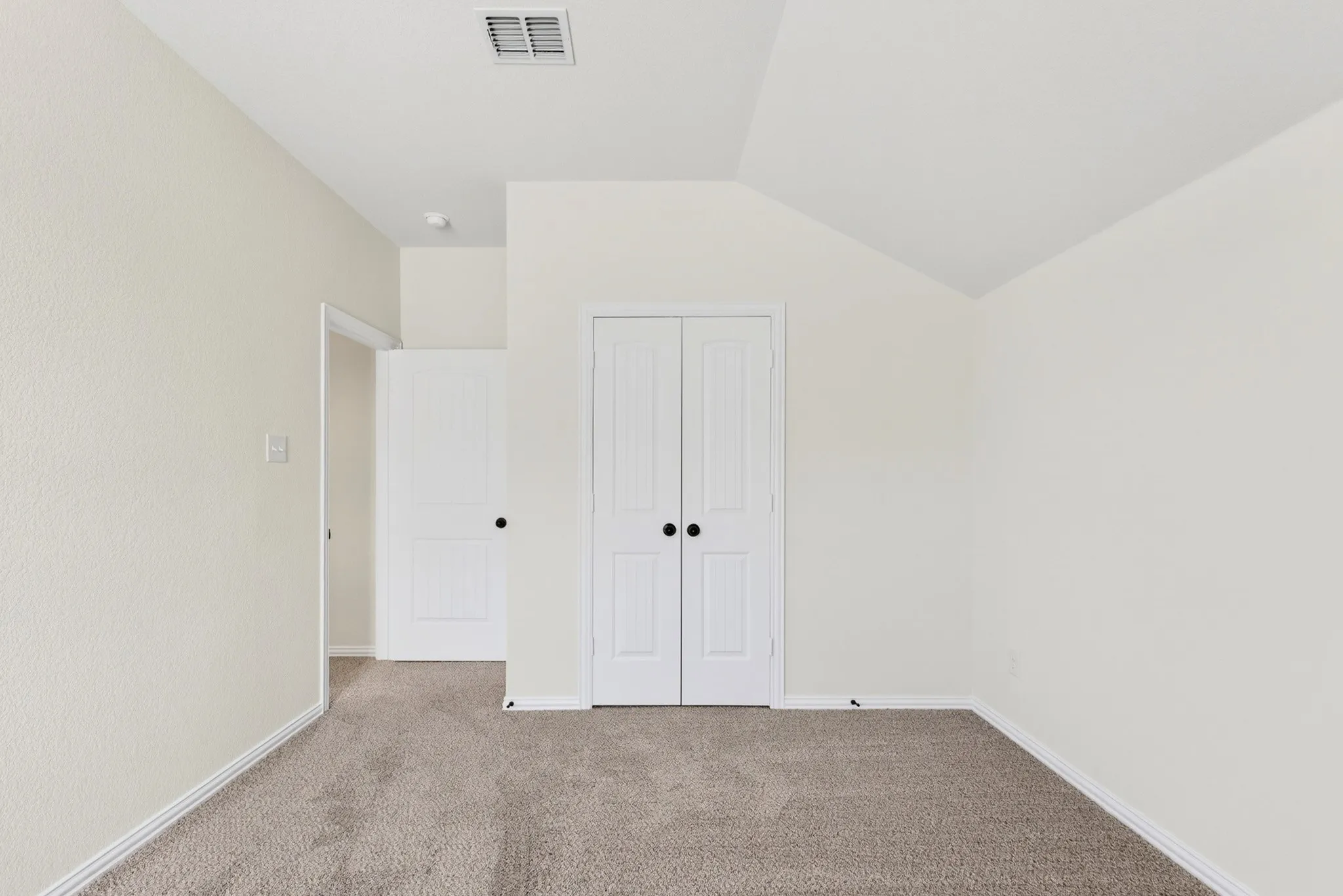 Neutral wall finishes, textured carpeting, vaulted ceiling, white interior doors, and black hardware