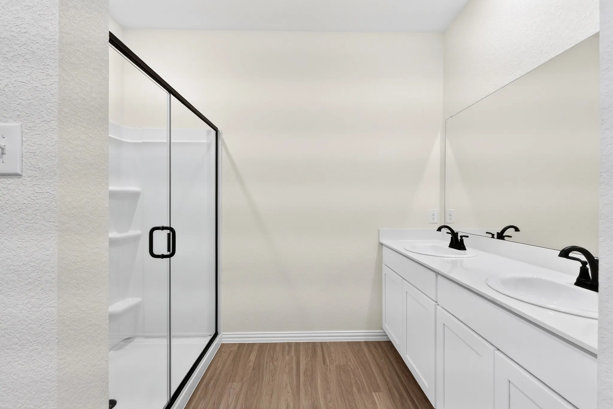Framed glass shower with built-in shelving, dual sink vanity with white cabinetry, matte black fixtures, and wood-finish flooring