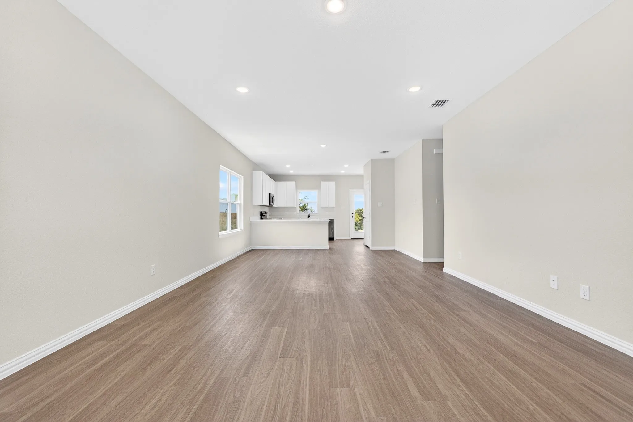 Open-concept living space featuring wood-finish flooring, recessed lighting, and a kitchen with white cabinetry and a breakfast bar