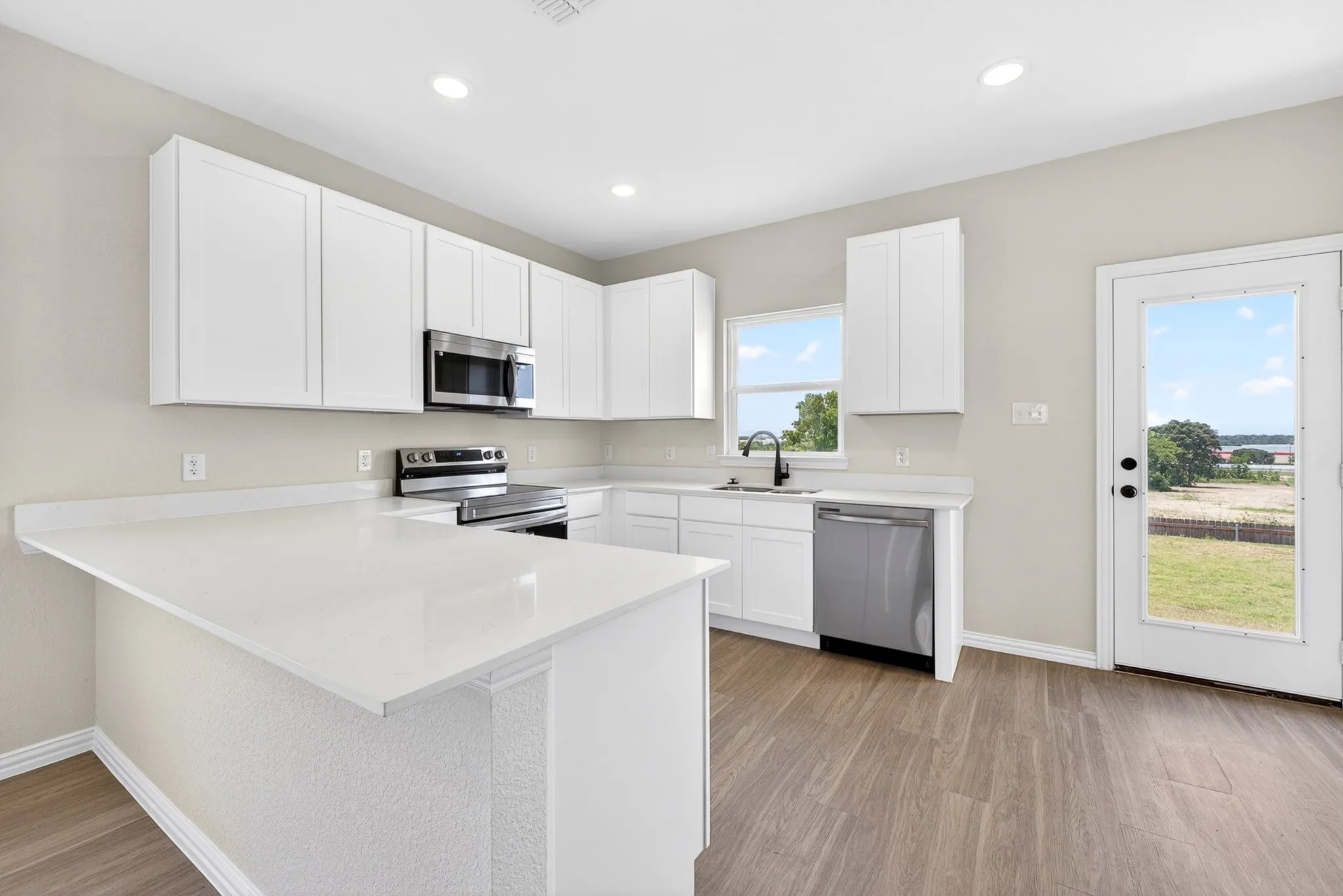 Kitchen featuring white cabinetry, light-toned countertops, wood-finish flooring, stainless steel appliances, and recessed lighting