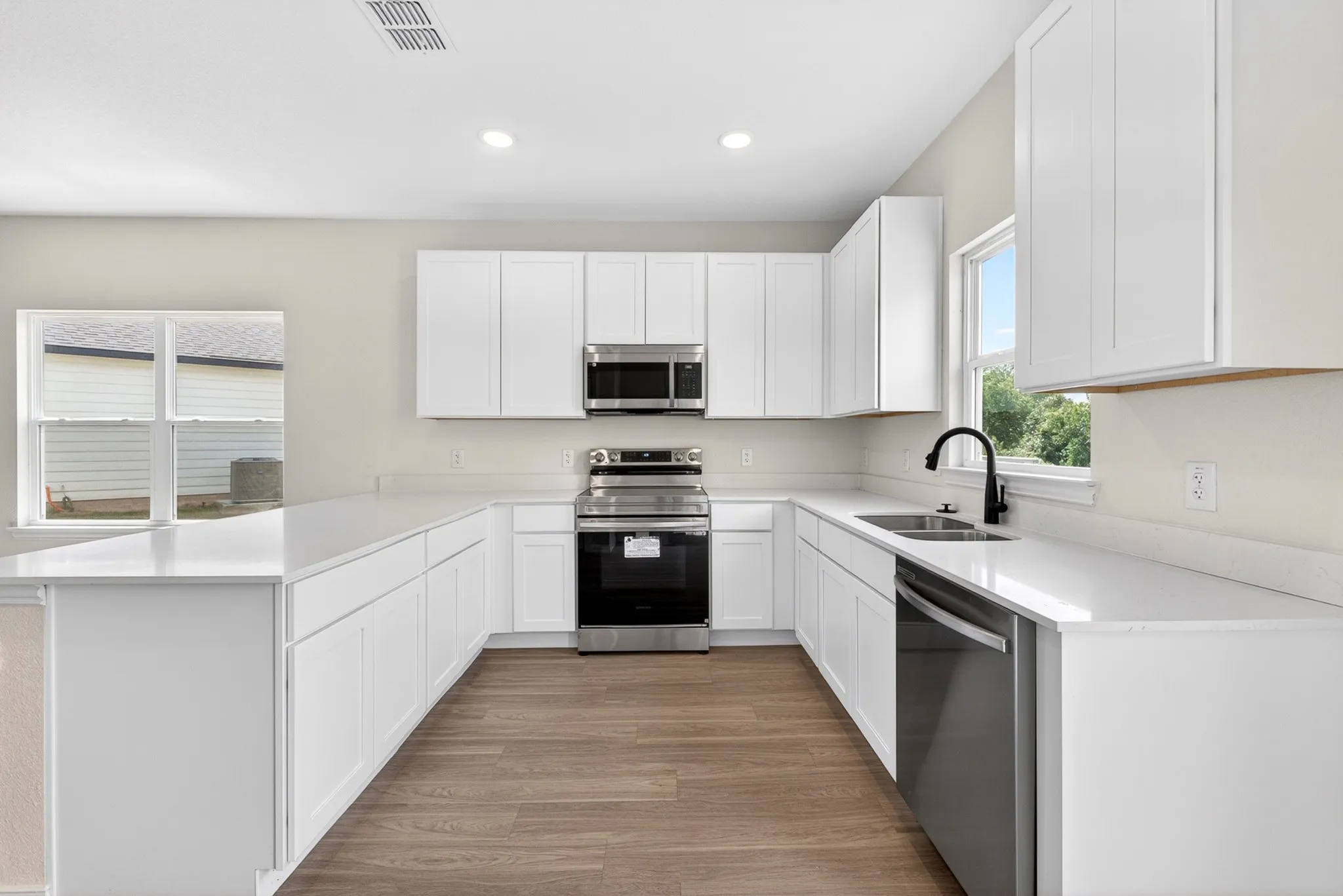U-shaped kitchen layout featuring white cabinetry, light countertops, wood-finish flooring, stainless steel appliances, and a matte black faucet