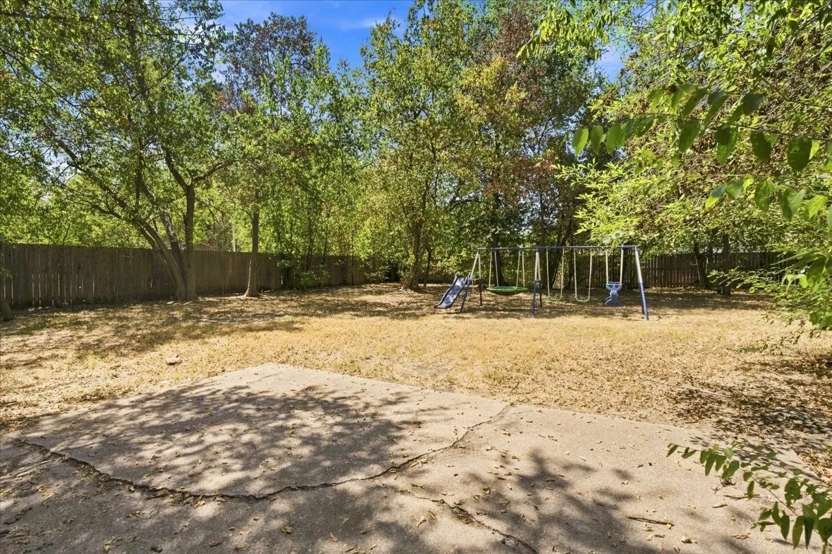 Expansive backyard featuring a privacy fence, mature trees, and a concrete patio