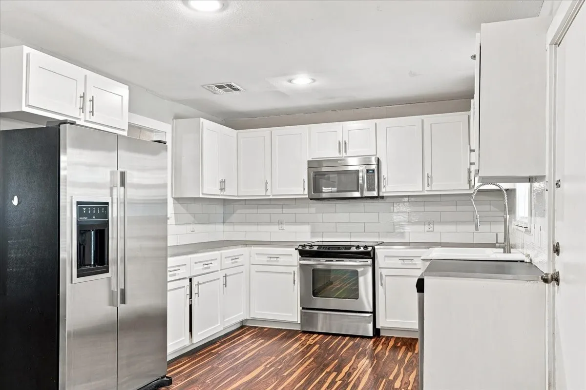 Modern kitchen featuring white shaker-style cabinetry, stainless steel appliances, subway tile backsplash, and wood-finish flooring