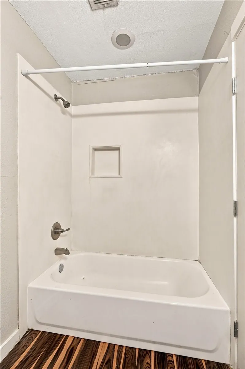 White bathtub with brushed nickel fixtures, a recessed wall niche, and wood-finish flooring