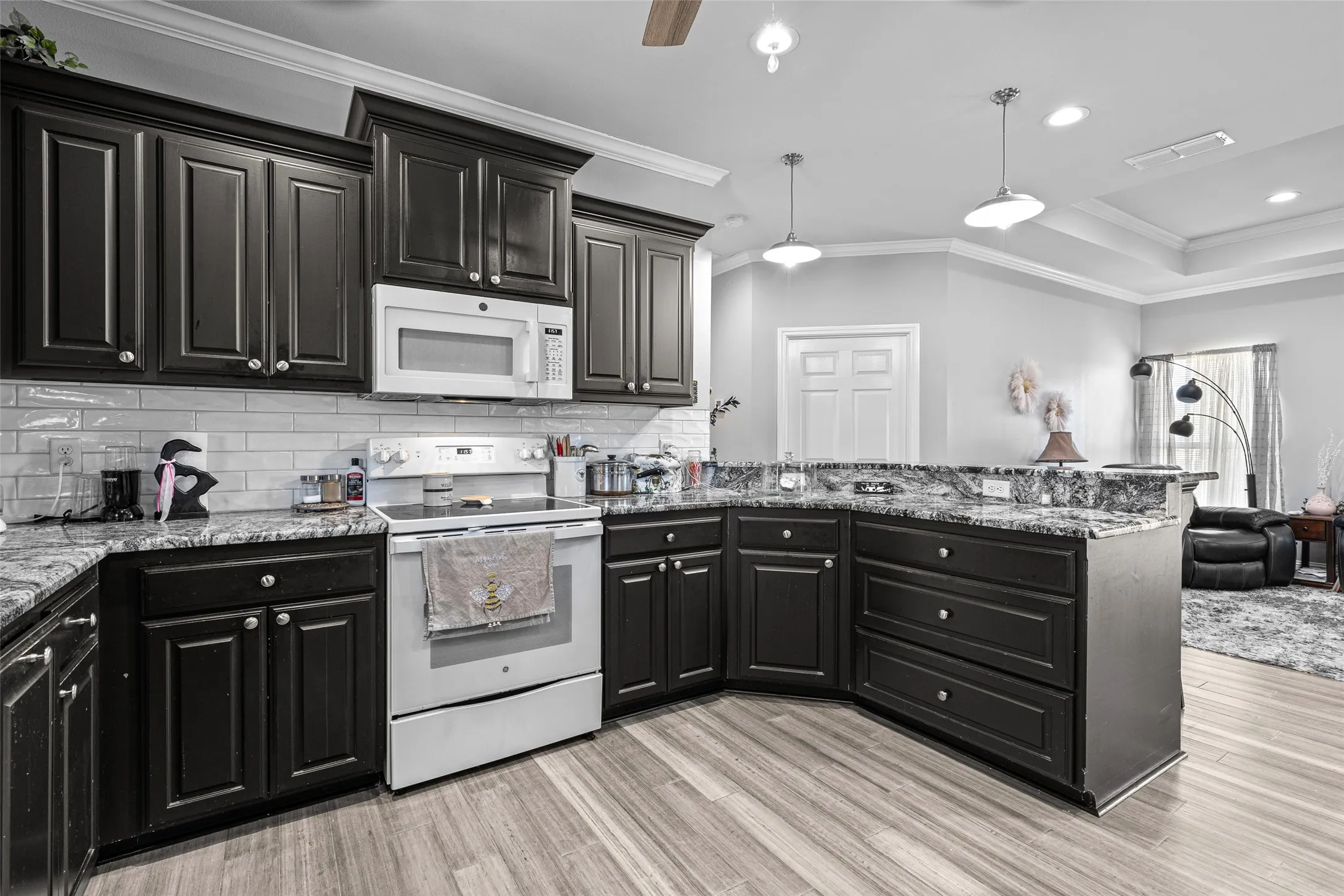Kitchen featuring pendant lighting, white appliances, light hardwood / wood-style flooring, backsplash, and ornamental molding