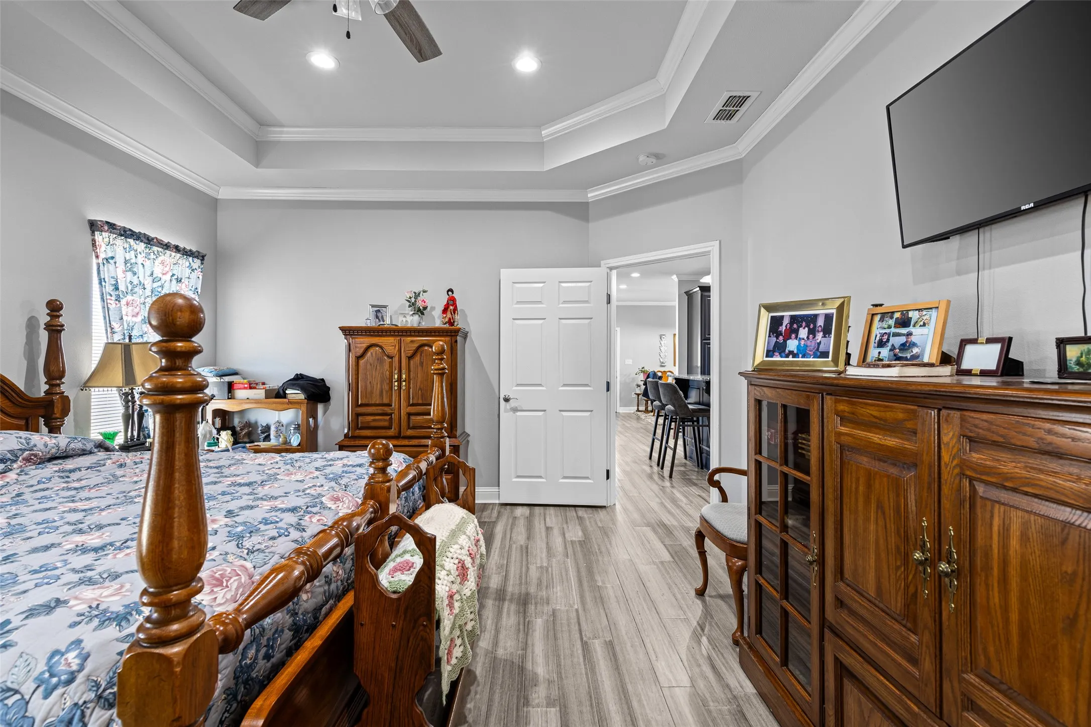 Bedroom with crown molding, light wood-type flooring, ceiling fan, and a tray ceiling