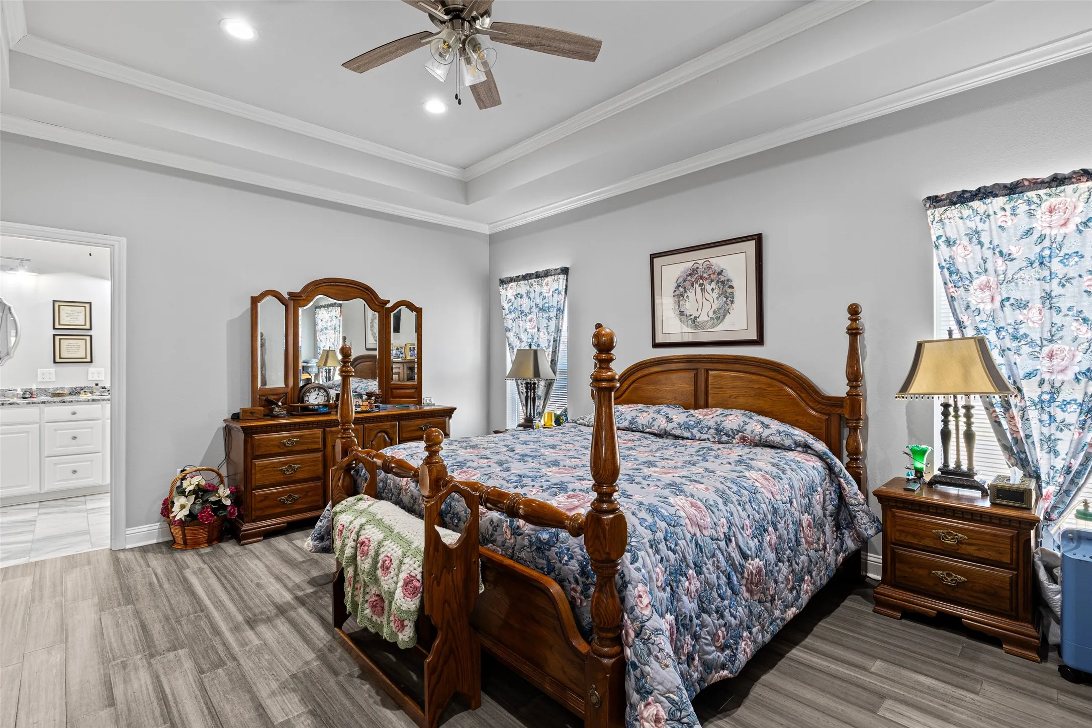 Bedroom with connected bathroom, ornamental molding, ceiling fan, a tray ceiling, and light wood-type flooring
