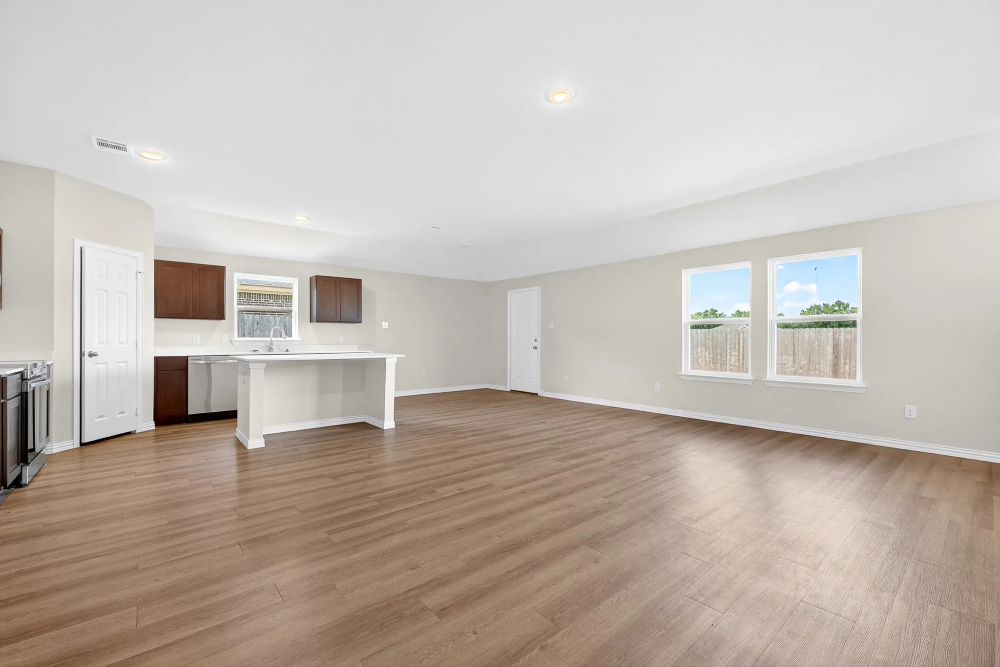 Open-concept living space with wood-finish flooring, a kitchen island, stainless steel appliances, and multiple windows