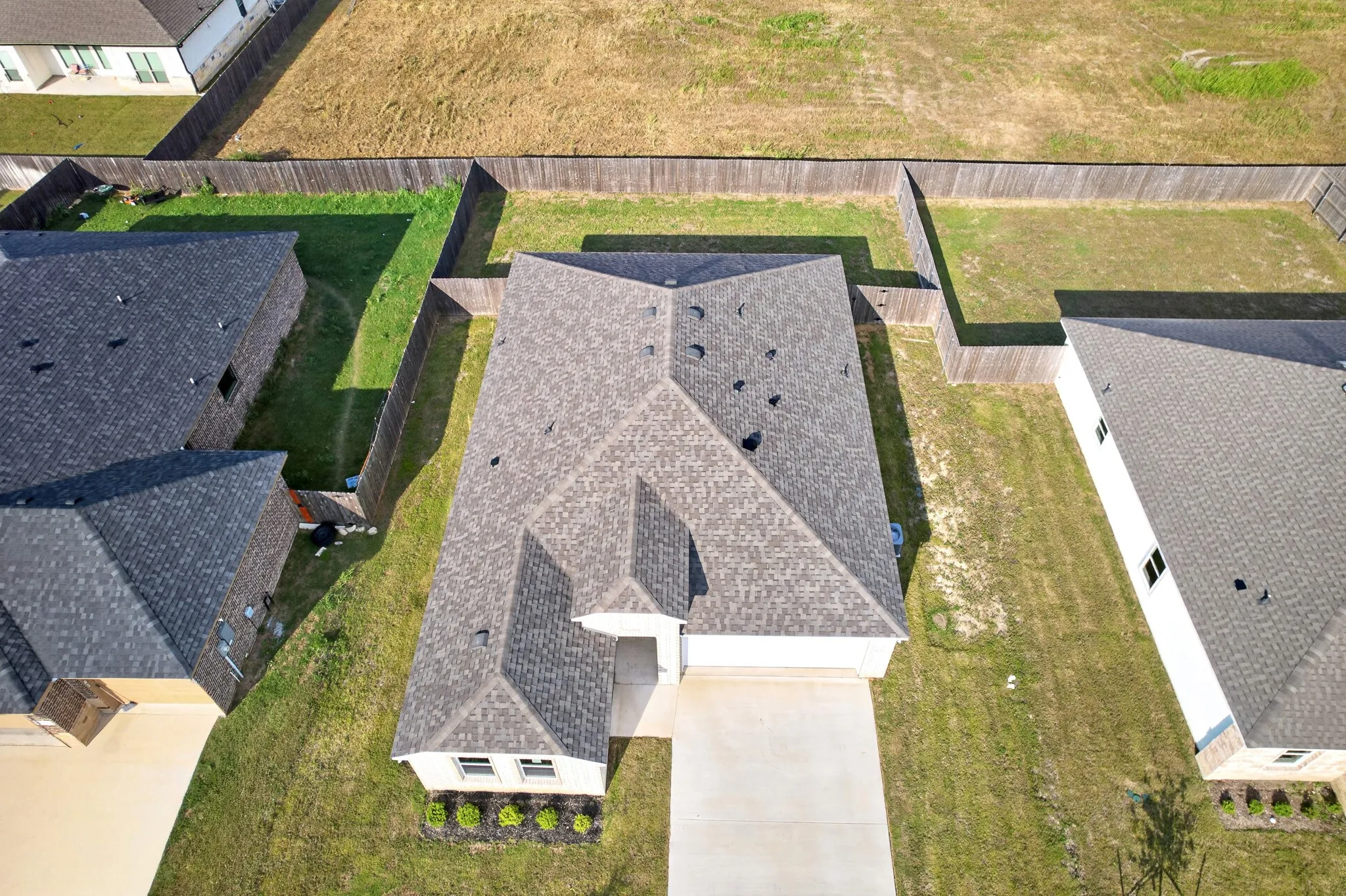 Pitched roofline, wood fencing, concrete driveway, front yard landscaping, and a side yard