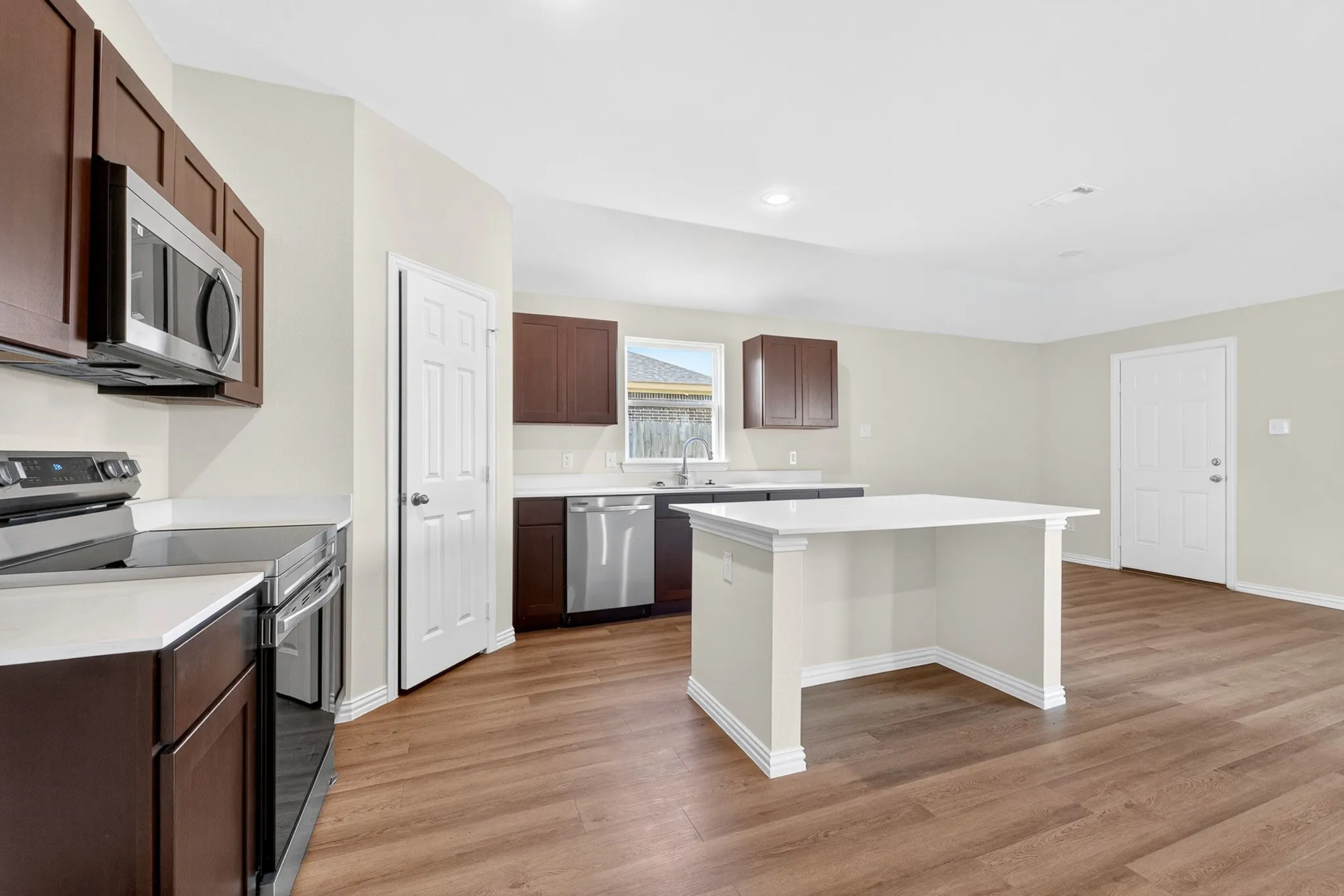 Kitchen featuring wood-finish flooring, white countertops, dark wood-finish cabinetry, and stainless steel appliances