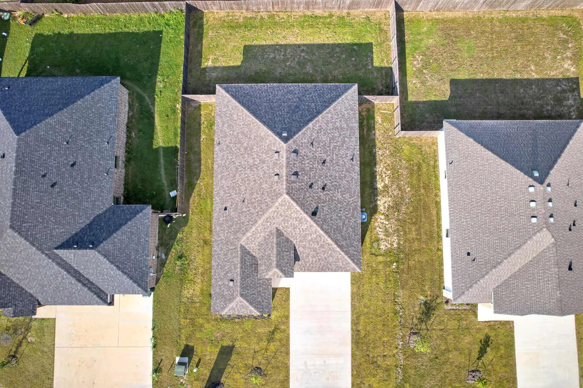 Pitched asphalt shingle roof, paved driveway, and perimeter fencing