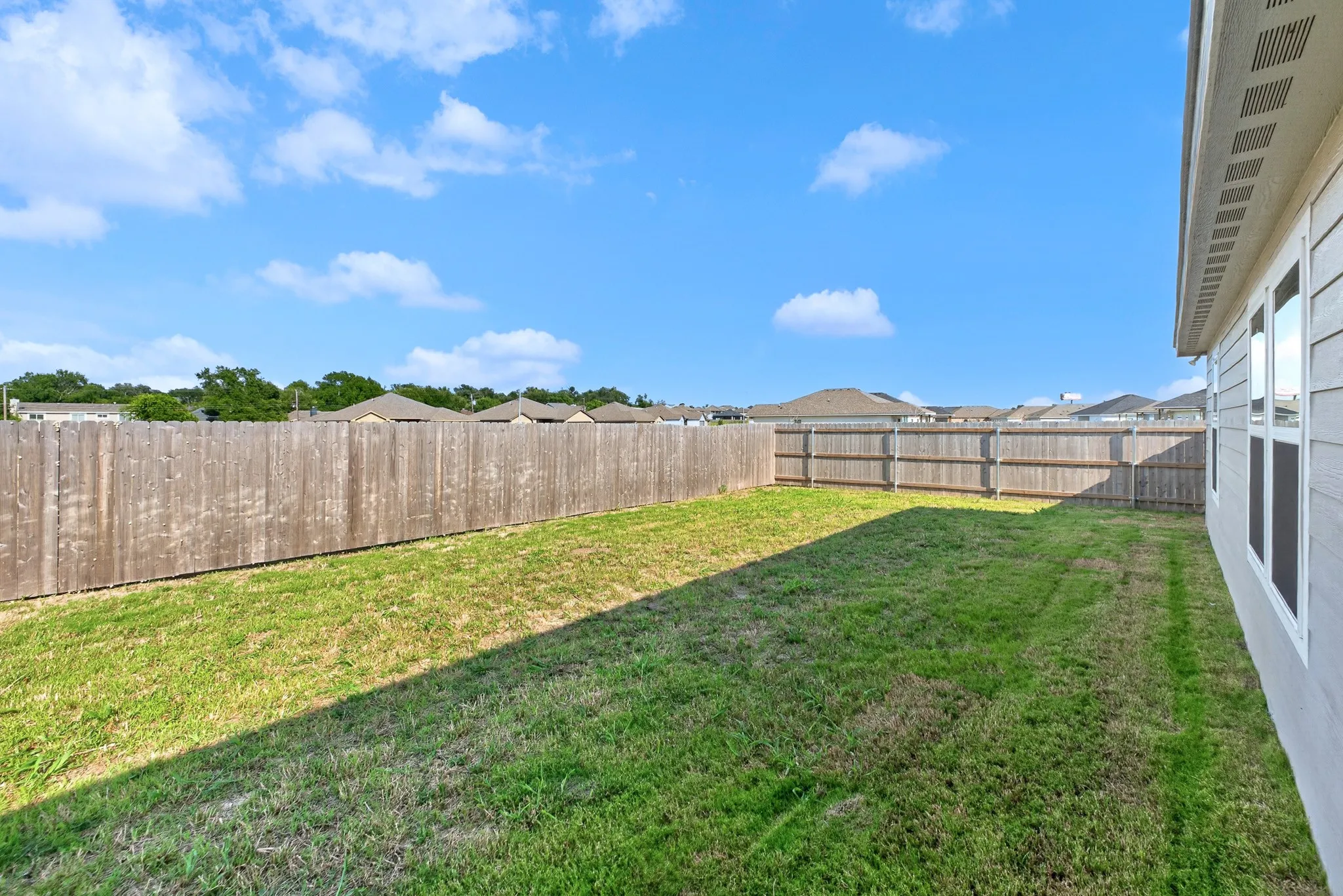 Expansive rear yard featuring a wooden privacy fence, natural grass, and a light-colored exterior wall with multiple windows