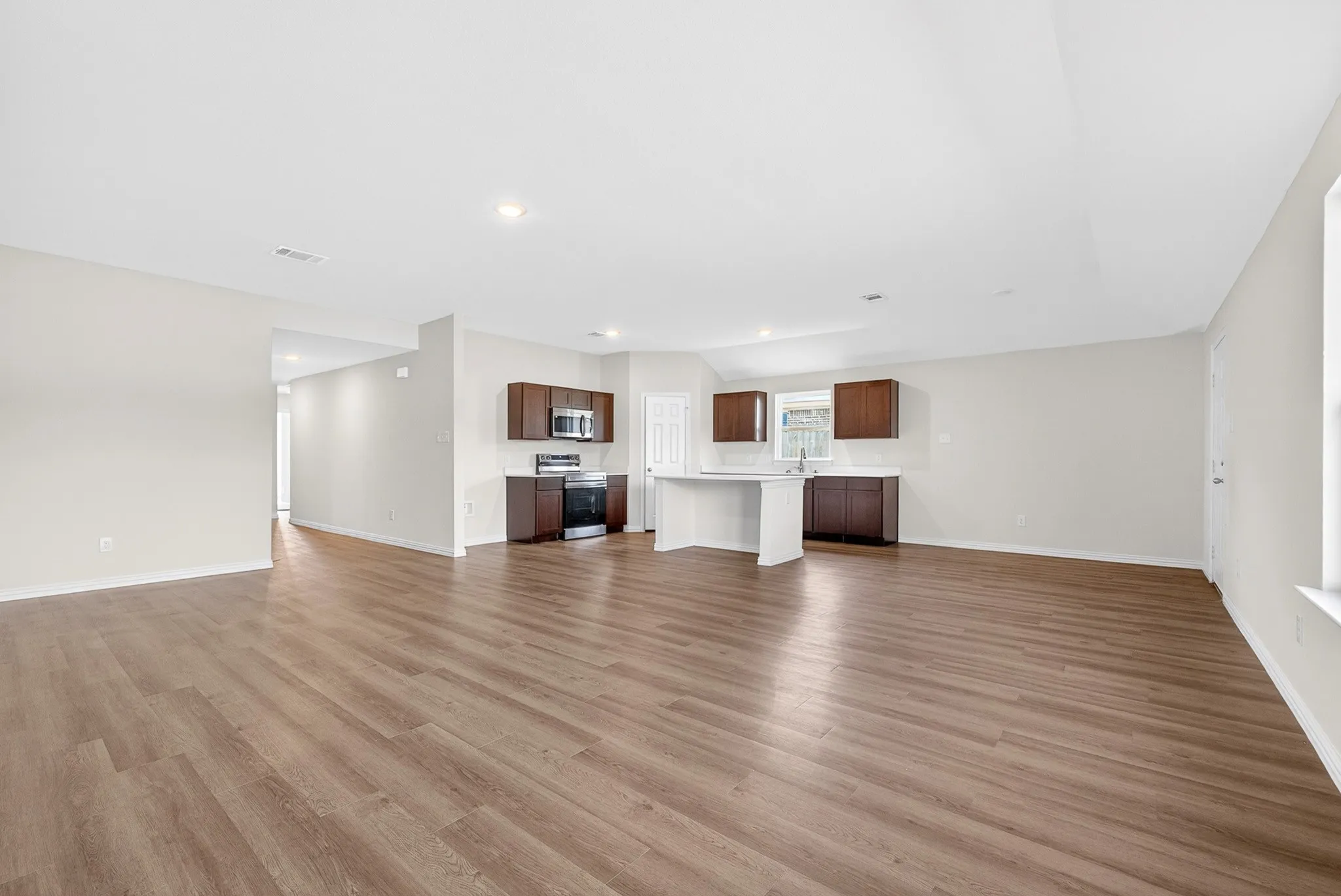 Open-concept living space with wood-finish flooring, recessed lighting, and a kitchen featuring stainless steel appliances, dark wood-finish cabinetry, and a light-toned island with a breakfast bar