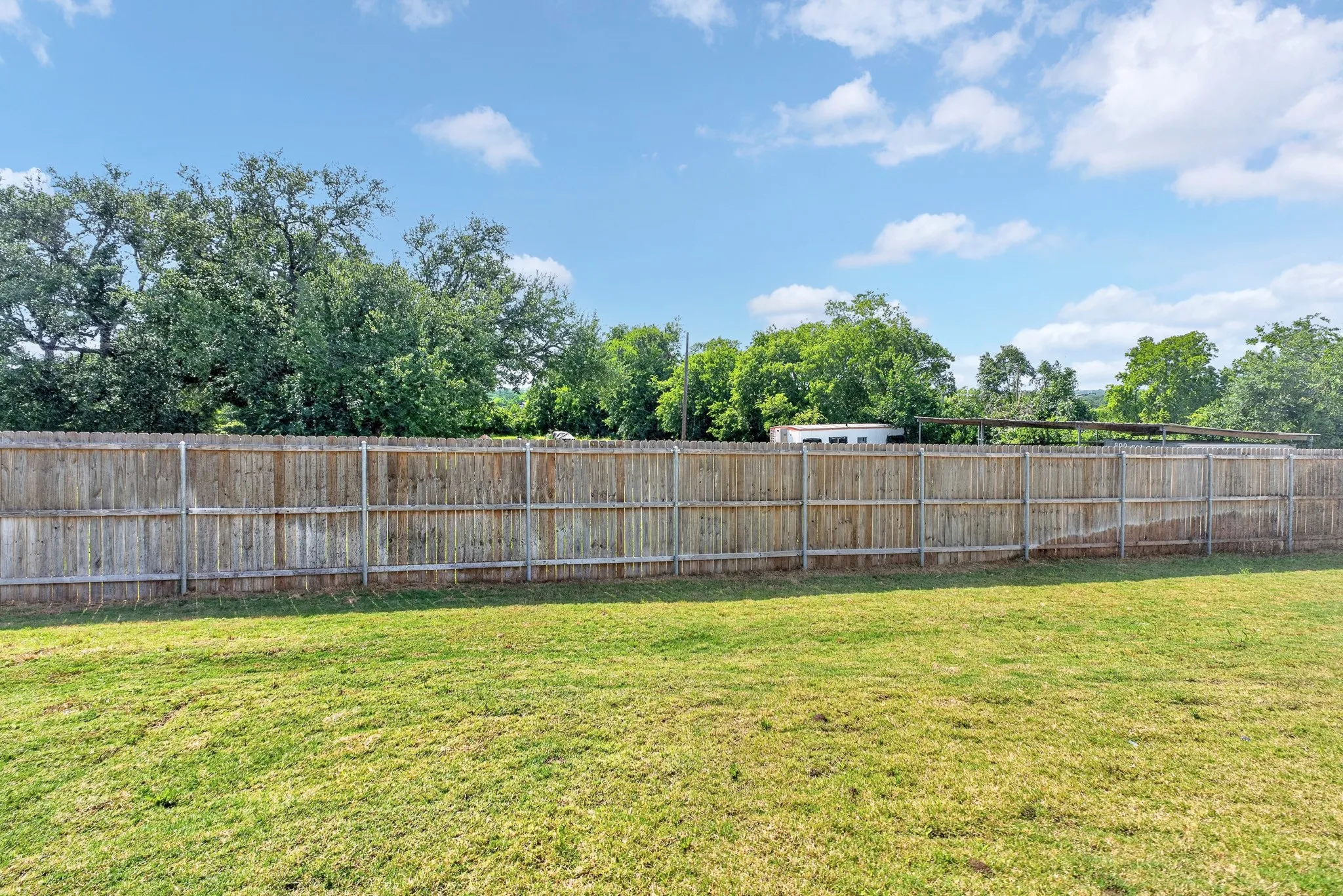 Expansive yard featuring a wooden privacy fence and mature trees