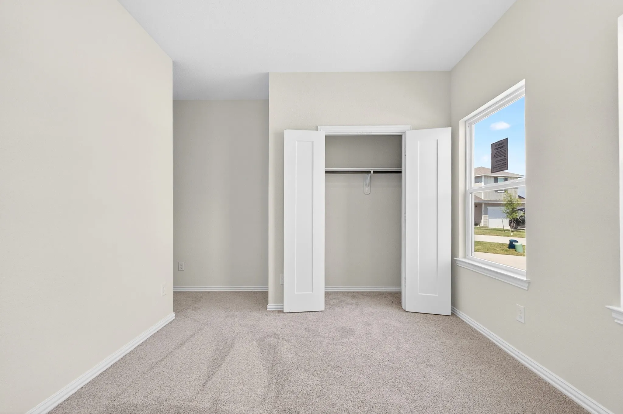 Light neutral wall color, plush carpeting, bi-fold closet doors, and a window with white trim
