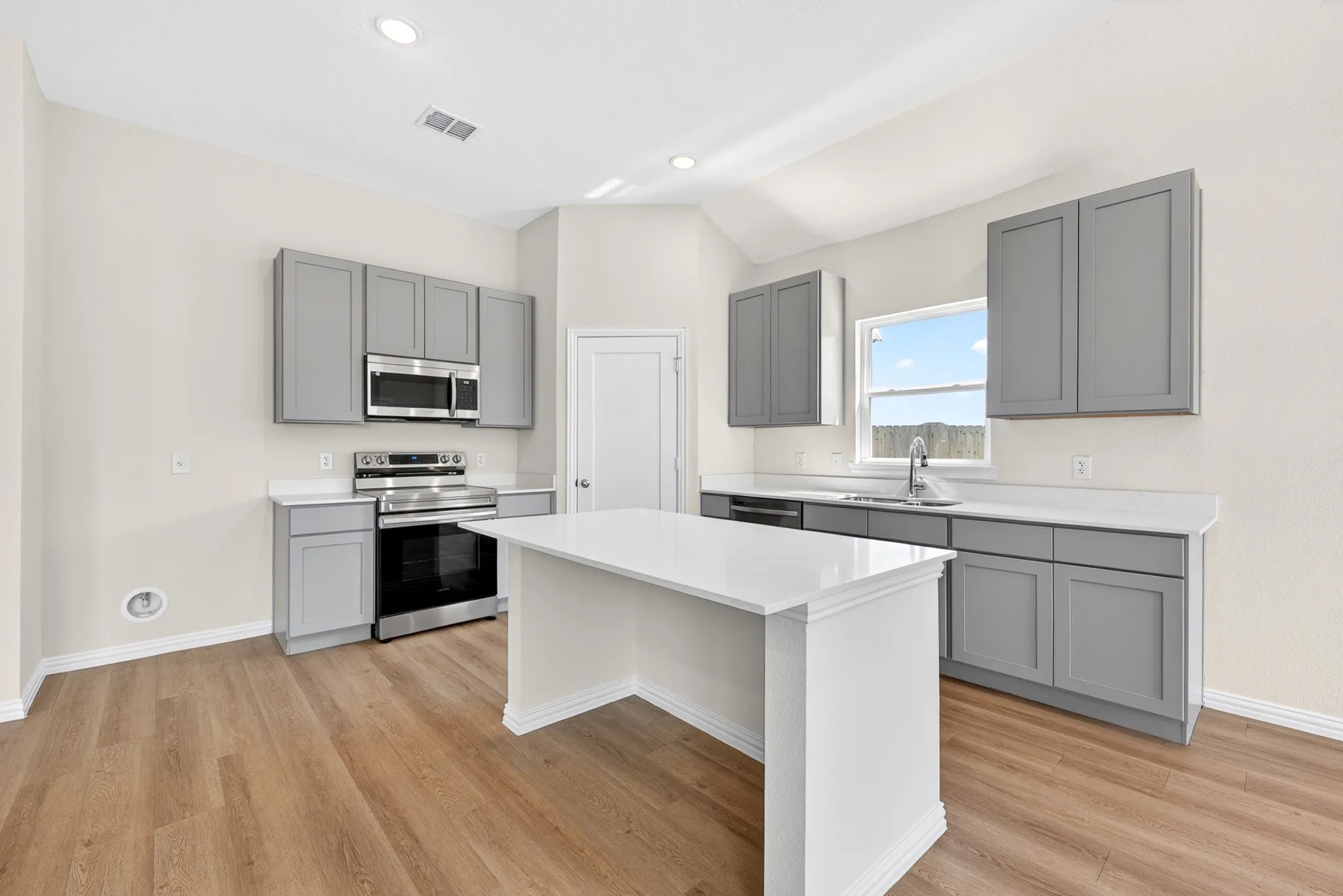 Kitchen featuring wood-finish flooring, white countertops, gray cabinetry, a central island, and stainless steel appliances