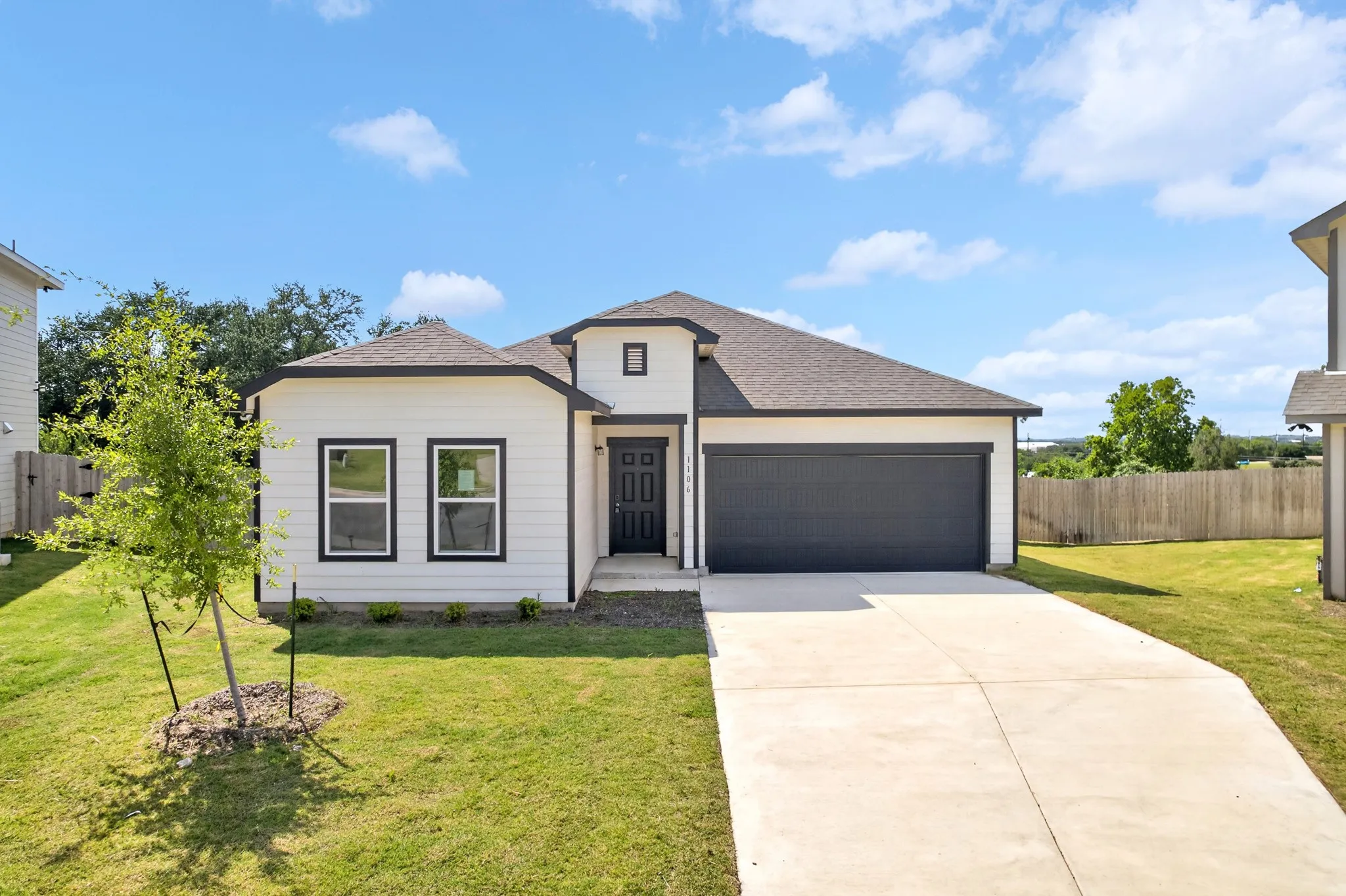 Contemporary exterior with white siding and dark trim, attached garage, concrete driveway, and front lawn