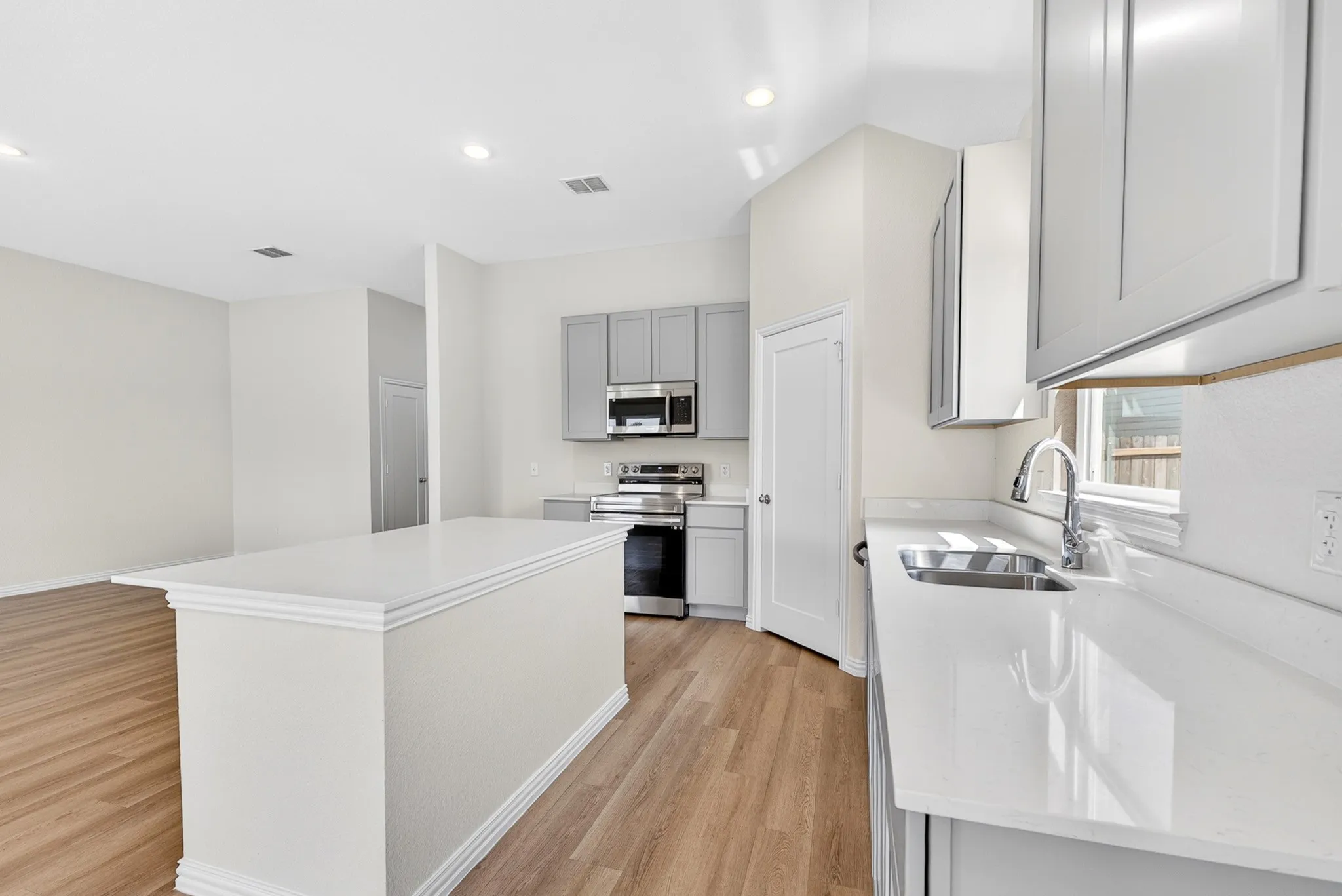 Kitchen featuring an expansive island with a white countertop, wood-finish flooring, gray cabinetry, stainless steel appliances, and recessed lighting