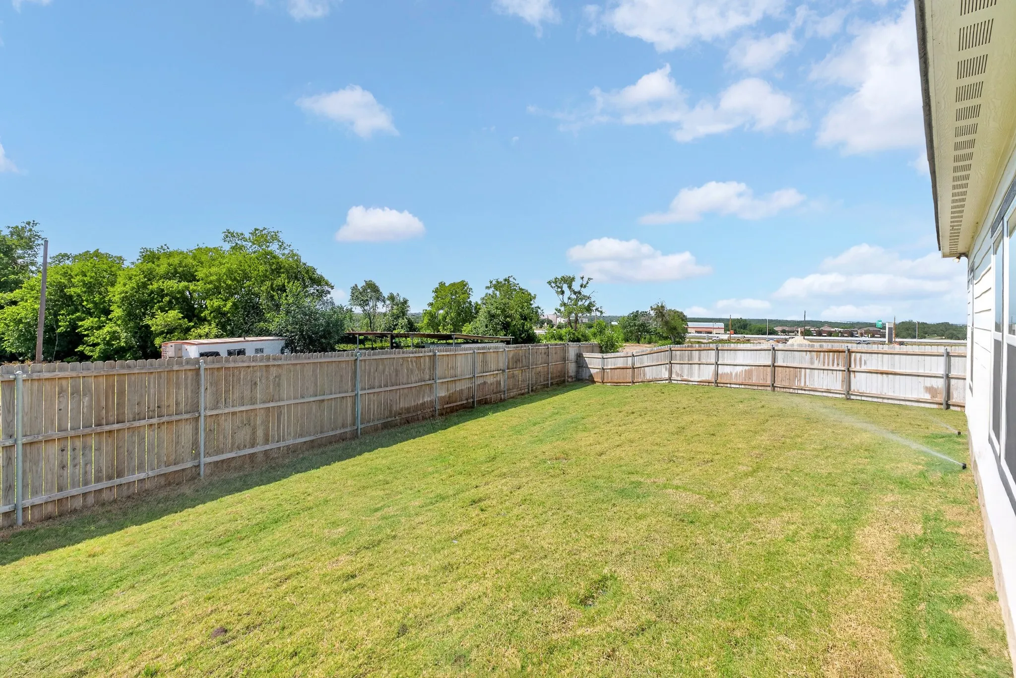 Expansive backyard with a full privacy fence, established lawn, and a side exterior wall with windows