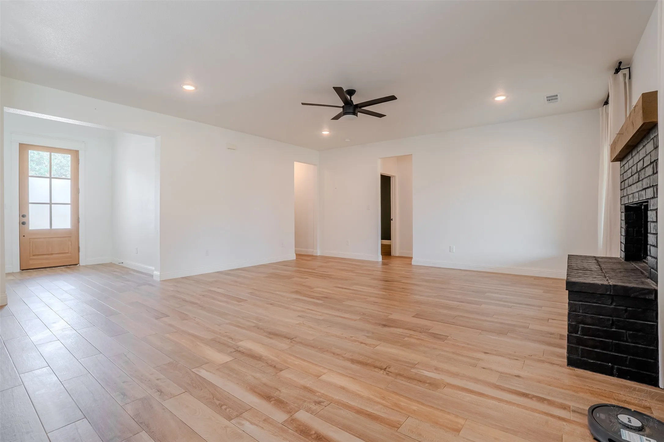 Expansive open-concept living area featuring wood-look tile flooring, a black brick fireplace with a wood mantle, and recessed lighting