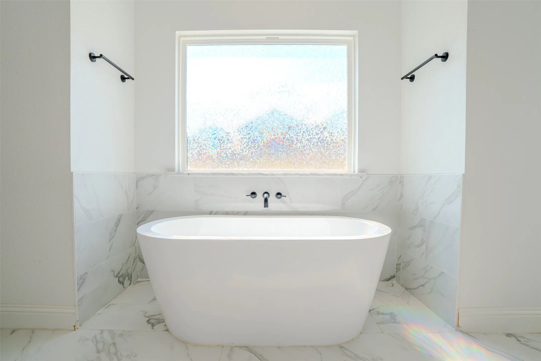 Freestanding soaking tub with a wall-mounted faucet, complemented by marble-look tile wall and floor tile