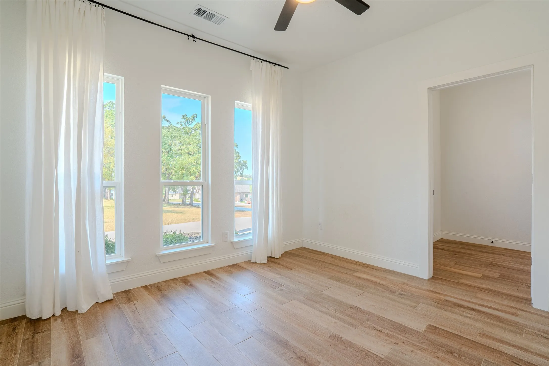 Bright well lit office/flex room with wood-look tile flooring located at the front of the structure right of the entry, multiple windows, a ceiling fan, and white walls