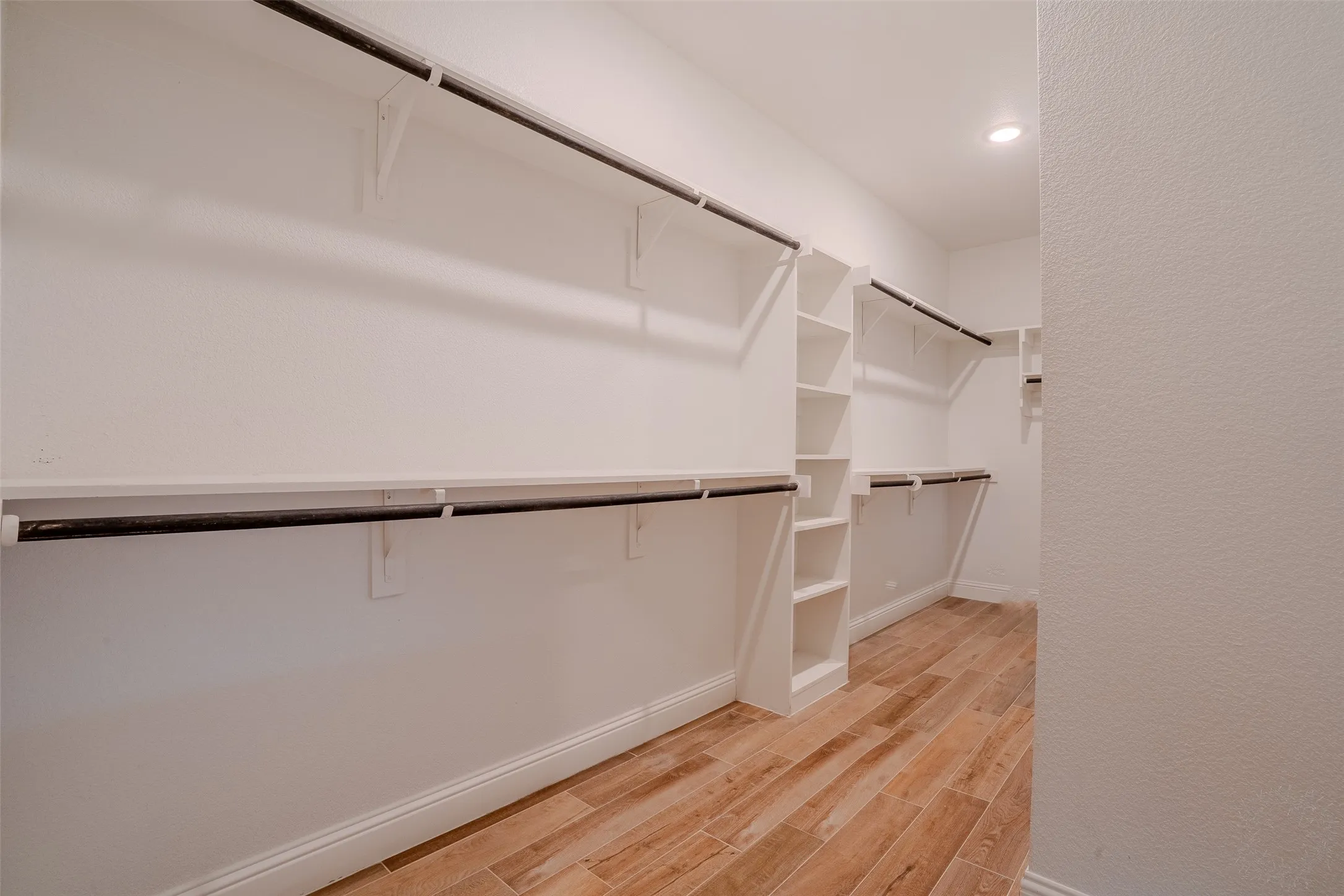 Spacious walk-in closet featuring wood-look tile flooring, recessed lighting, and extensive built-in shelving with hanging rods