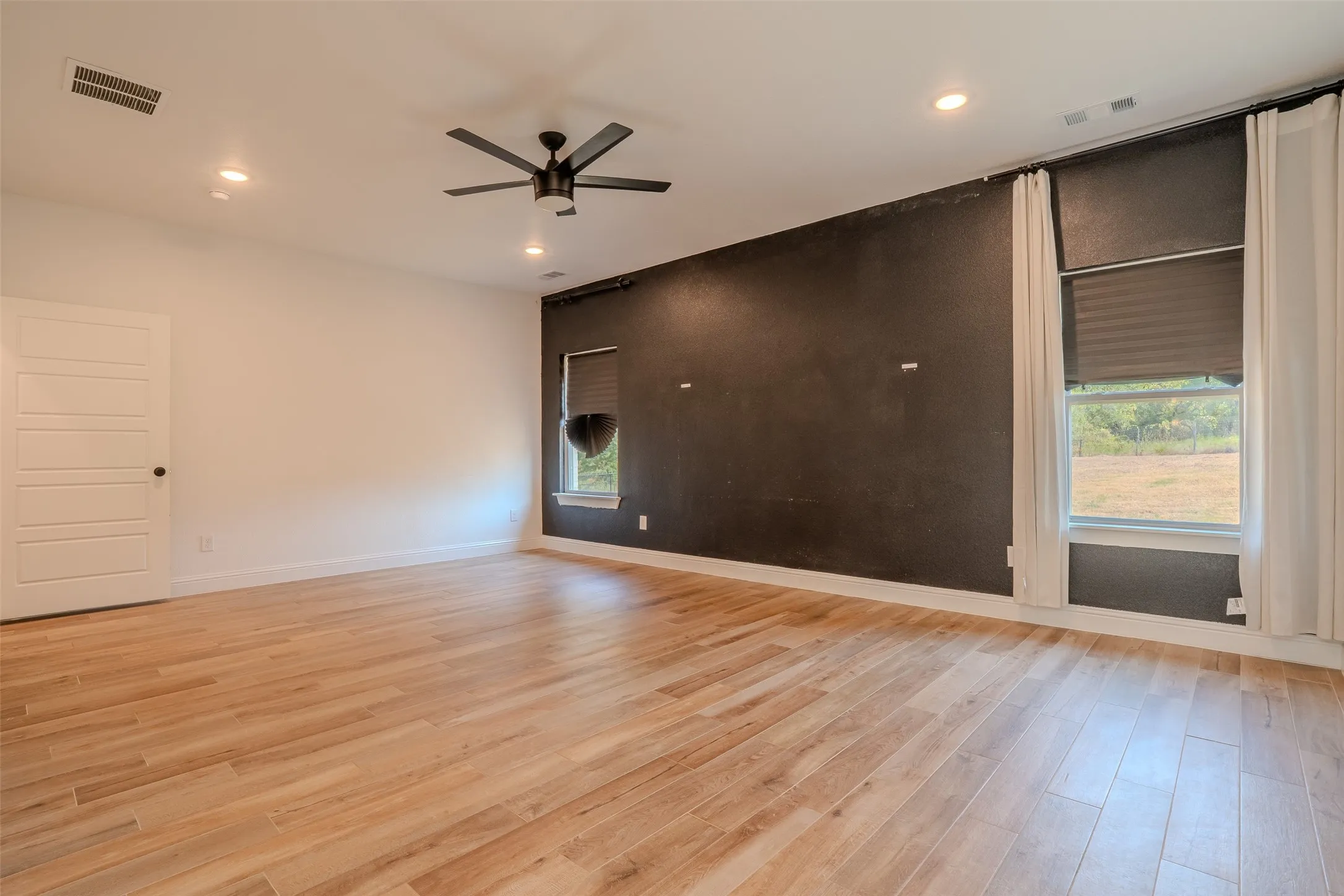 Massive Primary Bedroom, Recessed lighting, wood-look tile flooring, ceiling fan, and black accent wall.