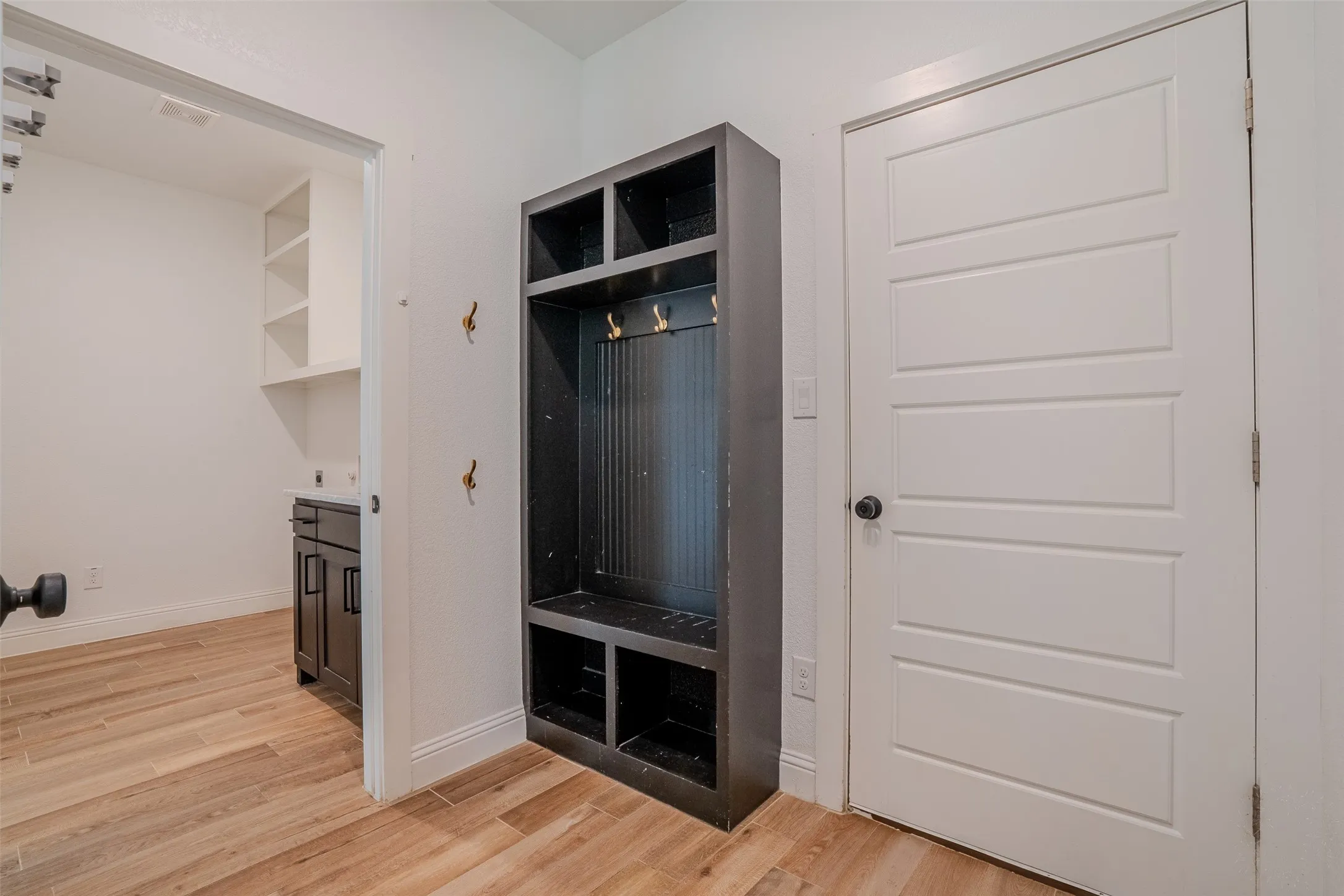 Wood-look tile flooring, built-in storage unit with hooks and shelving. Laundry room is visible to the left and garage access is to the right.