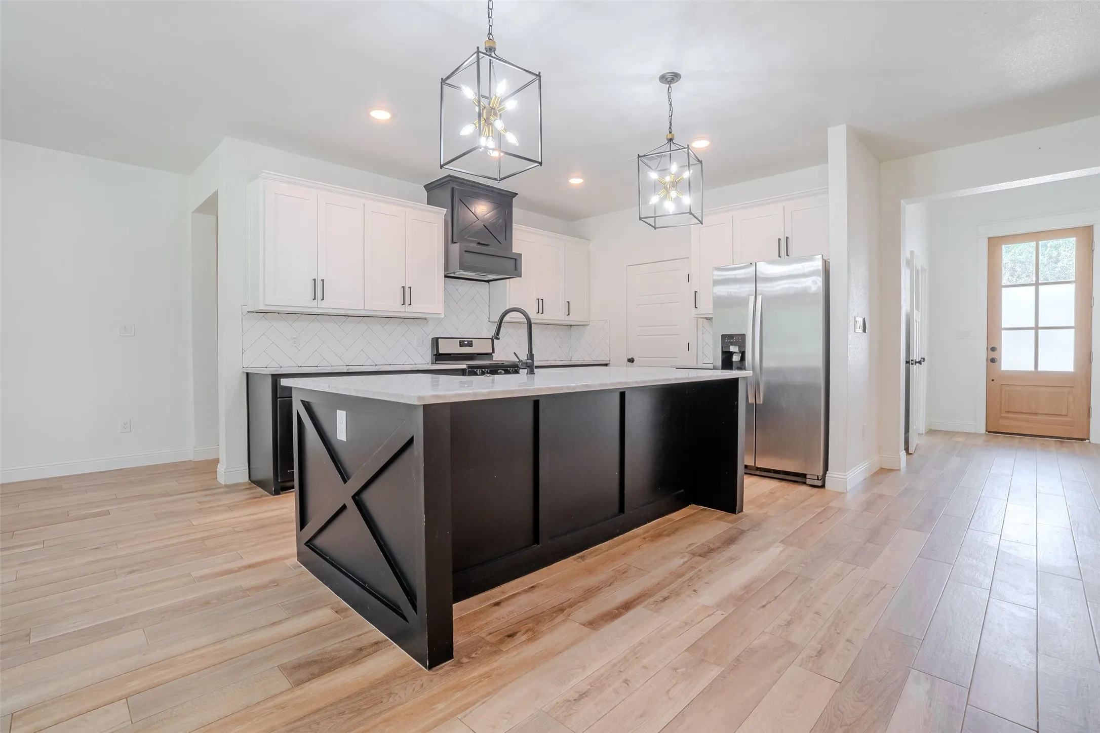 Kitchen featuring a large island with dark cabinetry, white upper cabinetry, stainless steel appliances, and wood-Look tile flooring, and white ceramic farmhouse stile sink.