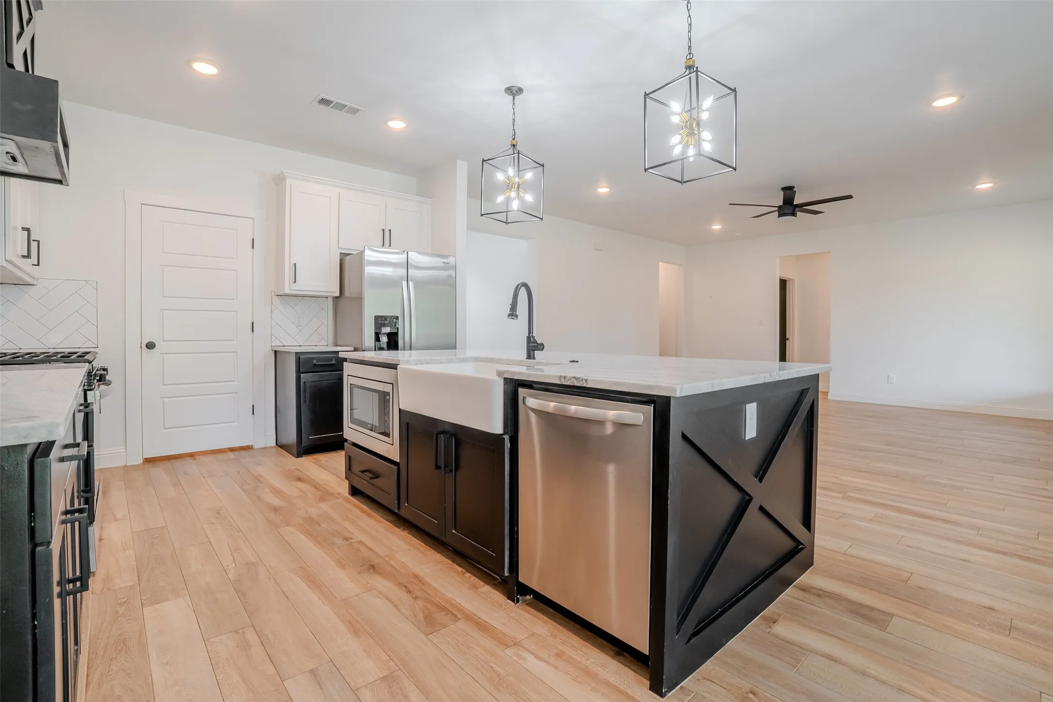 Kitchen island with a farmhouse sink, stainless steel appliances, light wood-finish flooring, white cabinetry, and recessed lighting