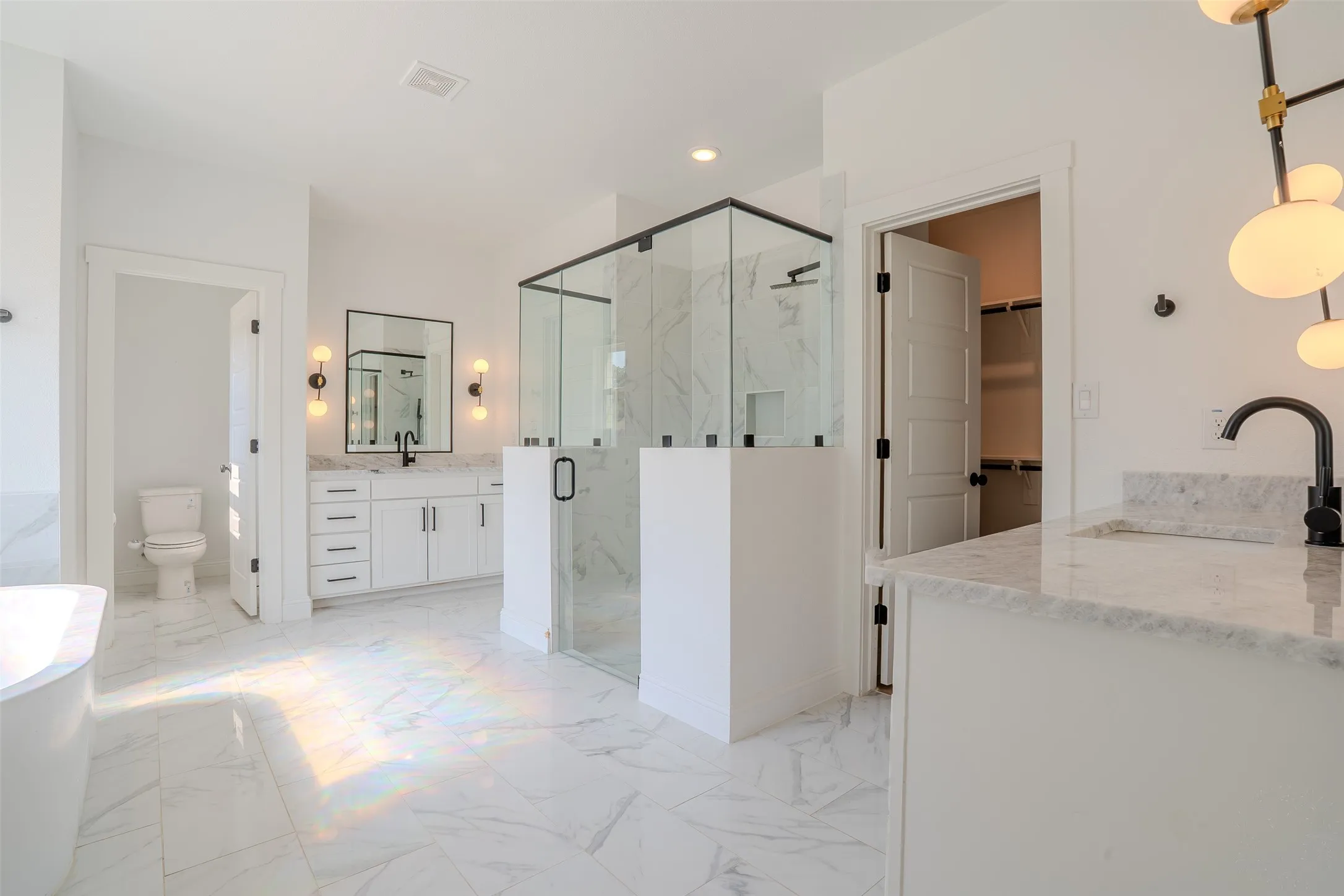 Dual vanity bathroom with white cabinetry, white granite countertops, and black fixtures. Glass Enclosed shower and a soaker tub underneath the large window. Dual closet access.