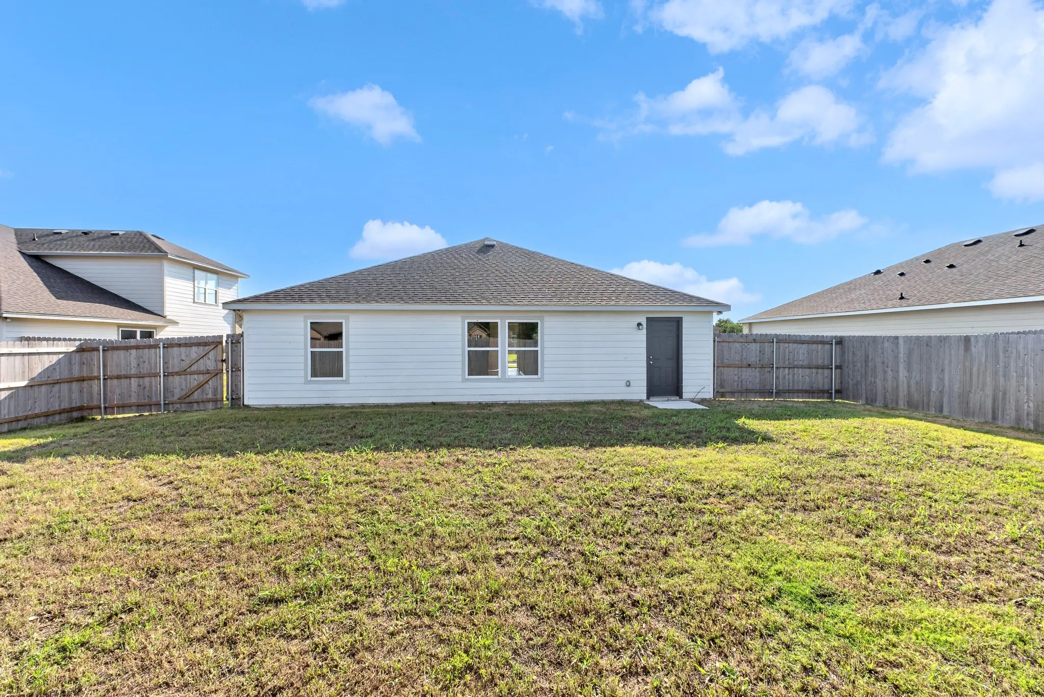 Expansive fenced backyard featuring a wood fence, white siding exterior, multiple windows, and a side entry door