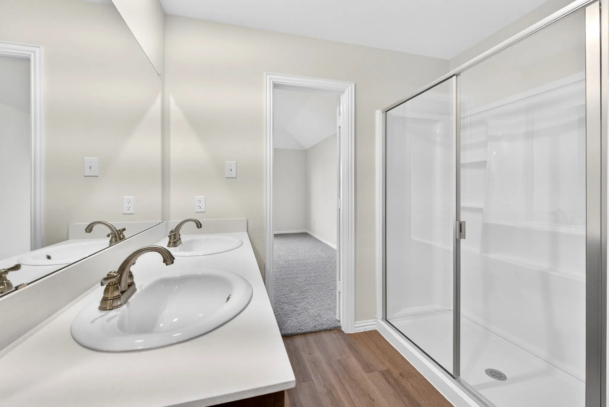 Dual vanity with white countertops, wood-finish flooring, and a glass-enclosed shower