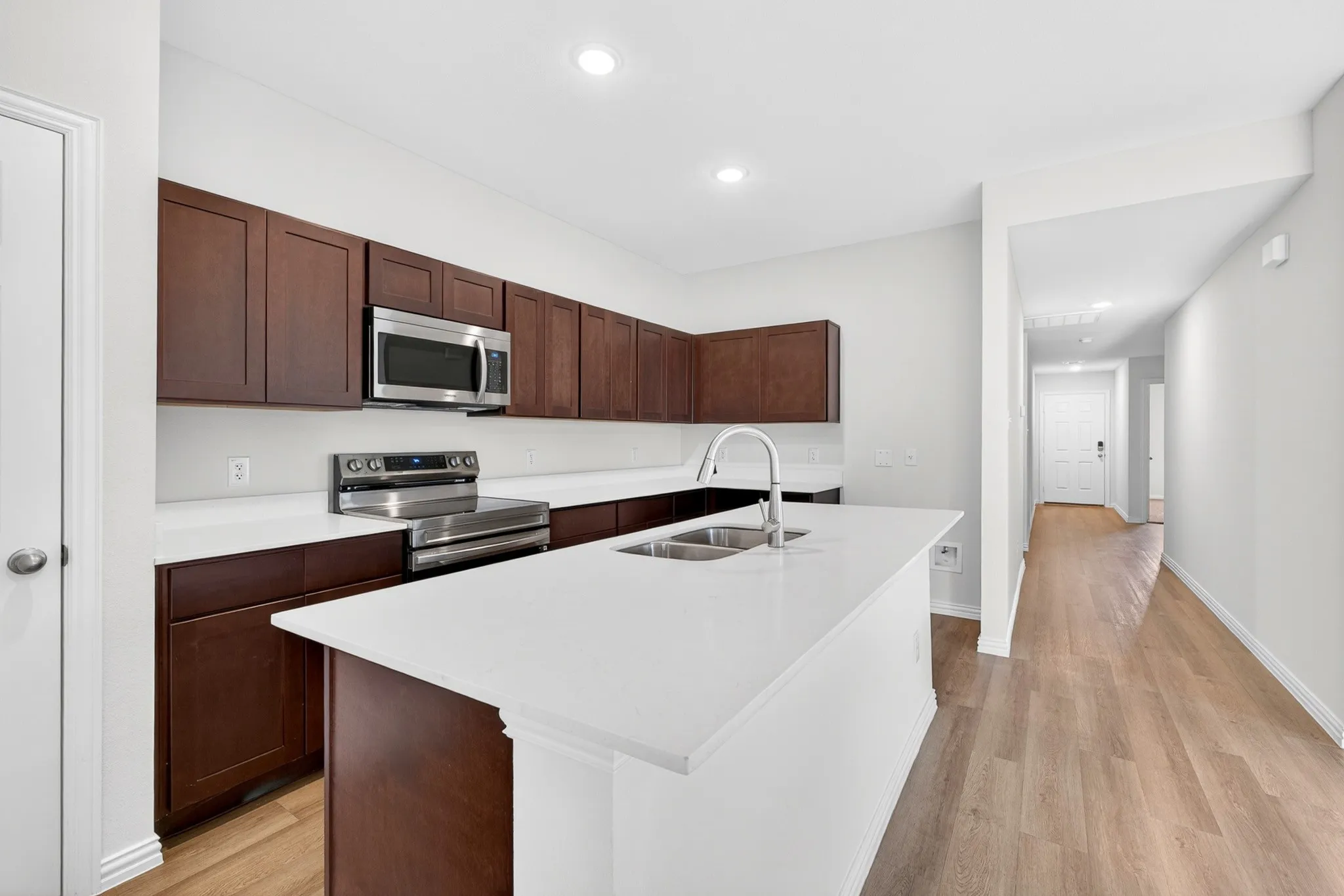 Kitchen featuring wood-finish flooring, dark wood cabinetry, white countertops, stainless steel appliances, and a kitchen island with an integrated sink