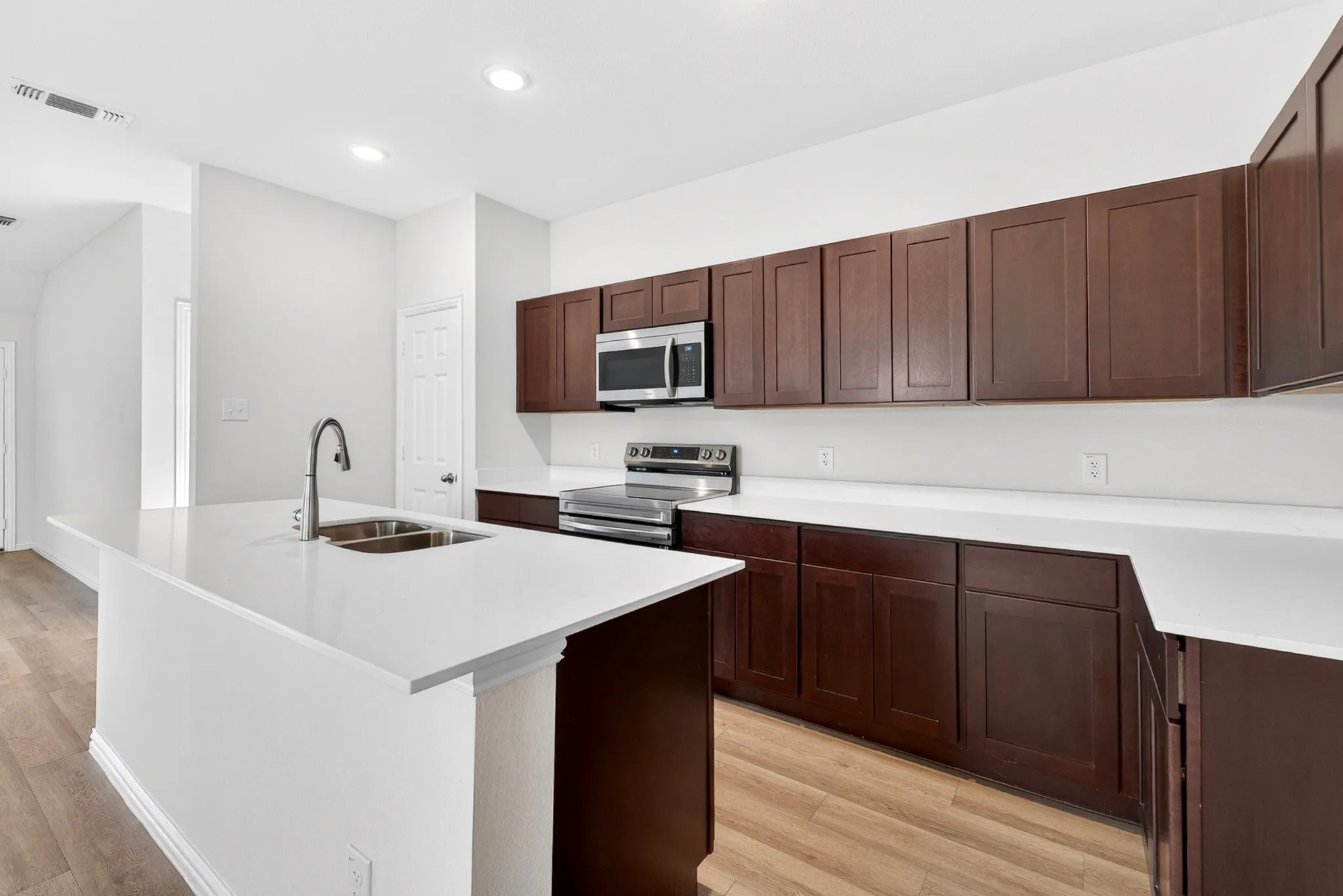 Kitchen featuring dark wood-finish cabinetry, stainless steel appliances, a center island with a double basin sink, and wood-finish flooring