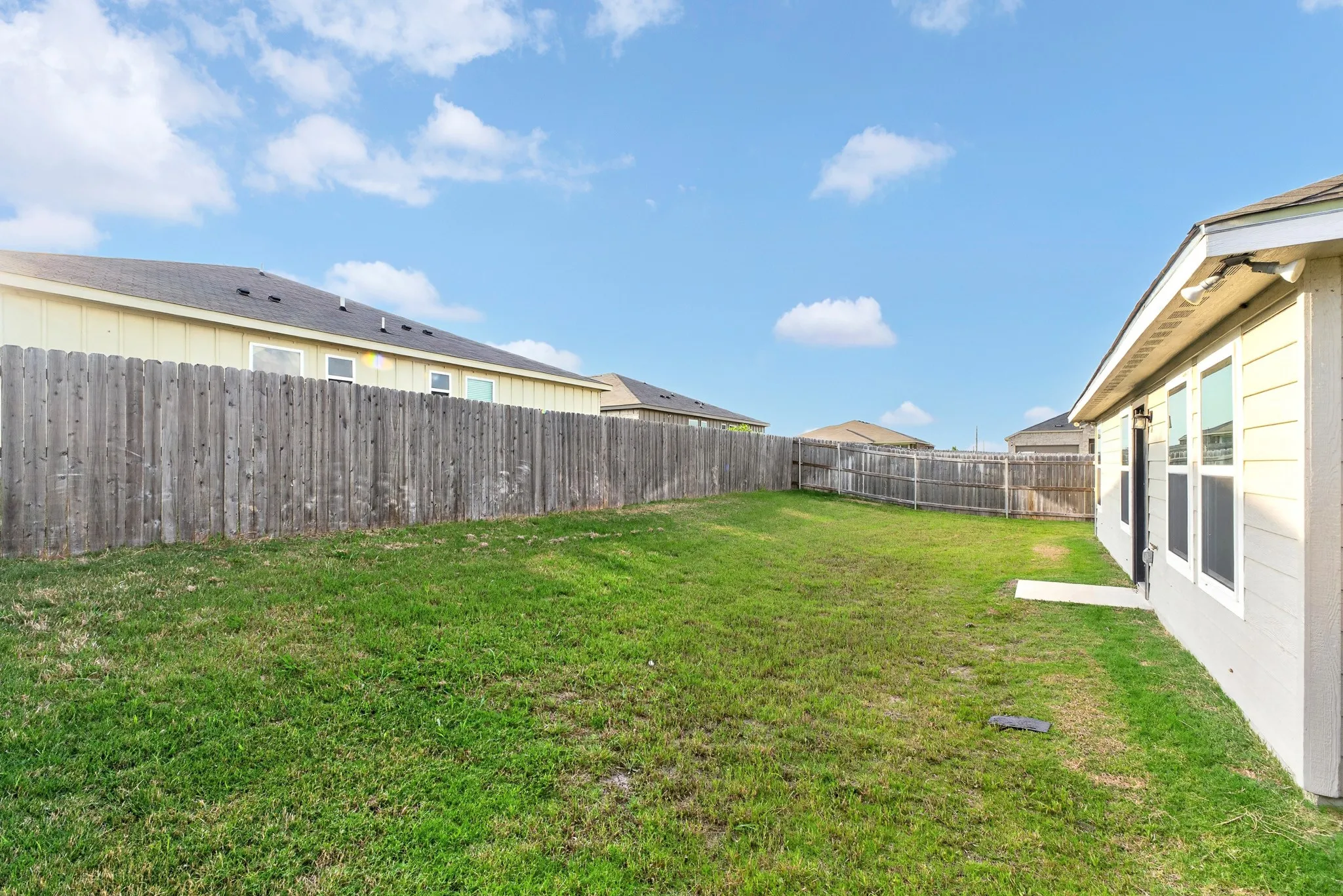 Expansive backyard with a manicured lawn, full privacy fencing, and a concrete patio
