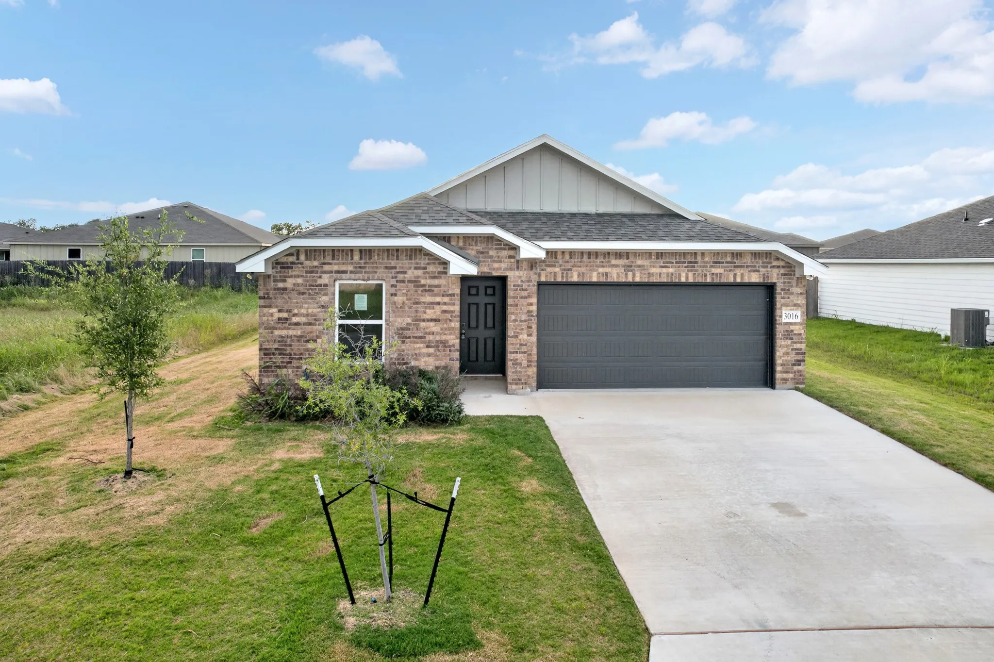 Brown brick exterior featuring a dark gray garage door, white trim, and a concrete driveway