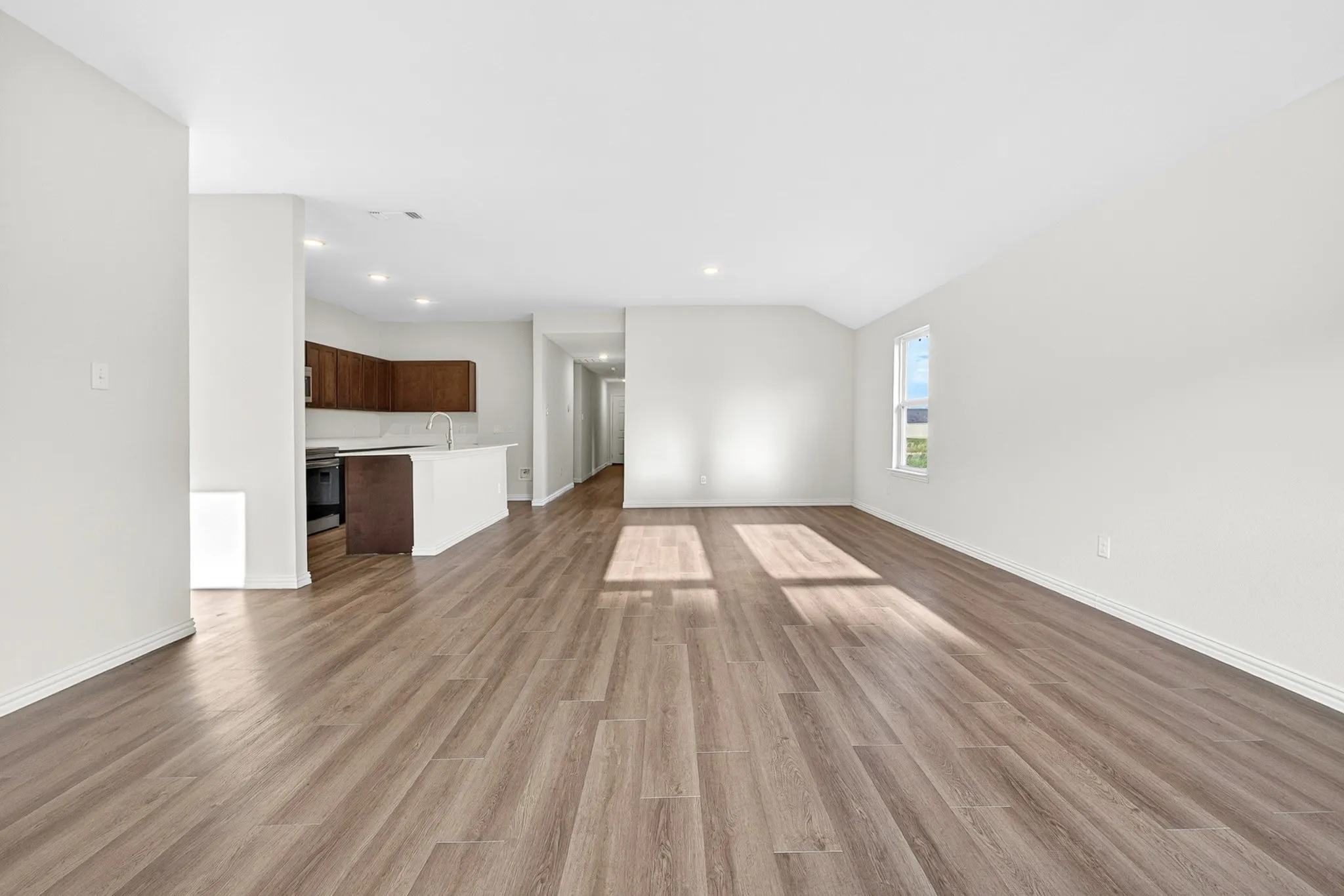 Expansive interior featuring wood-finish flooring, white walls, recessed lighting, and a kitchen with dark wood cabinetry and a white countertop