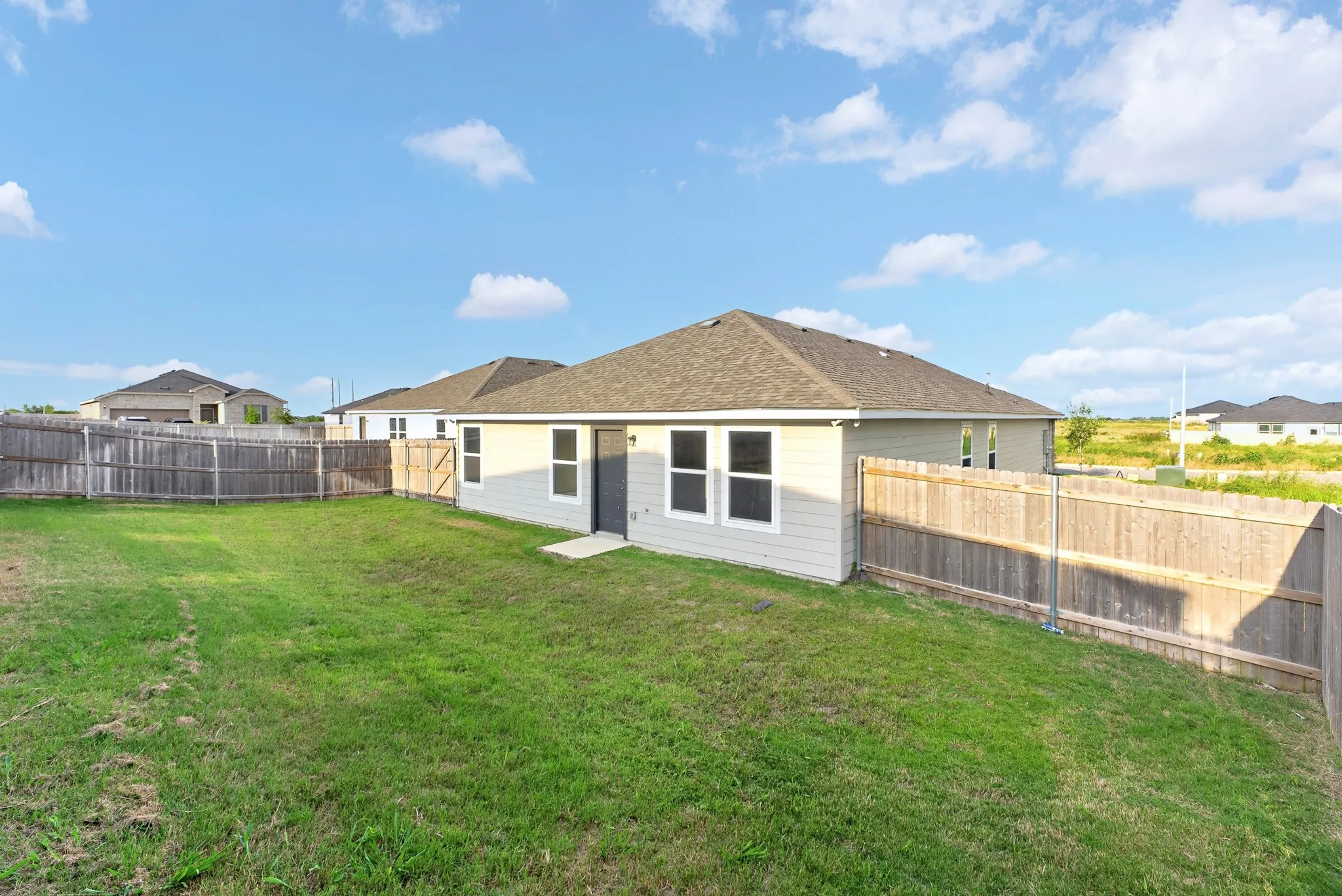 Expansive backyard featuring a privacy fence, manicured lawn, and a light-colored stucco exterior with multiple windows