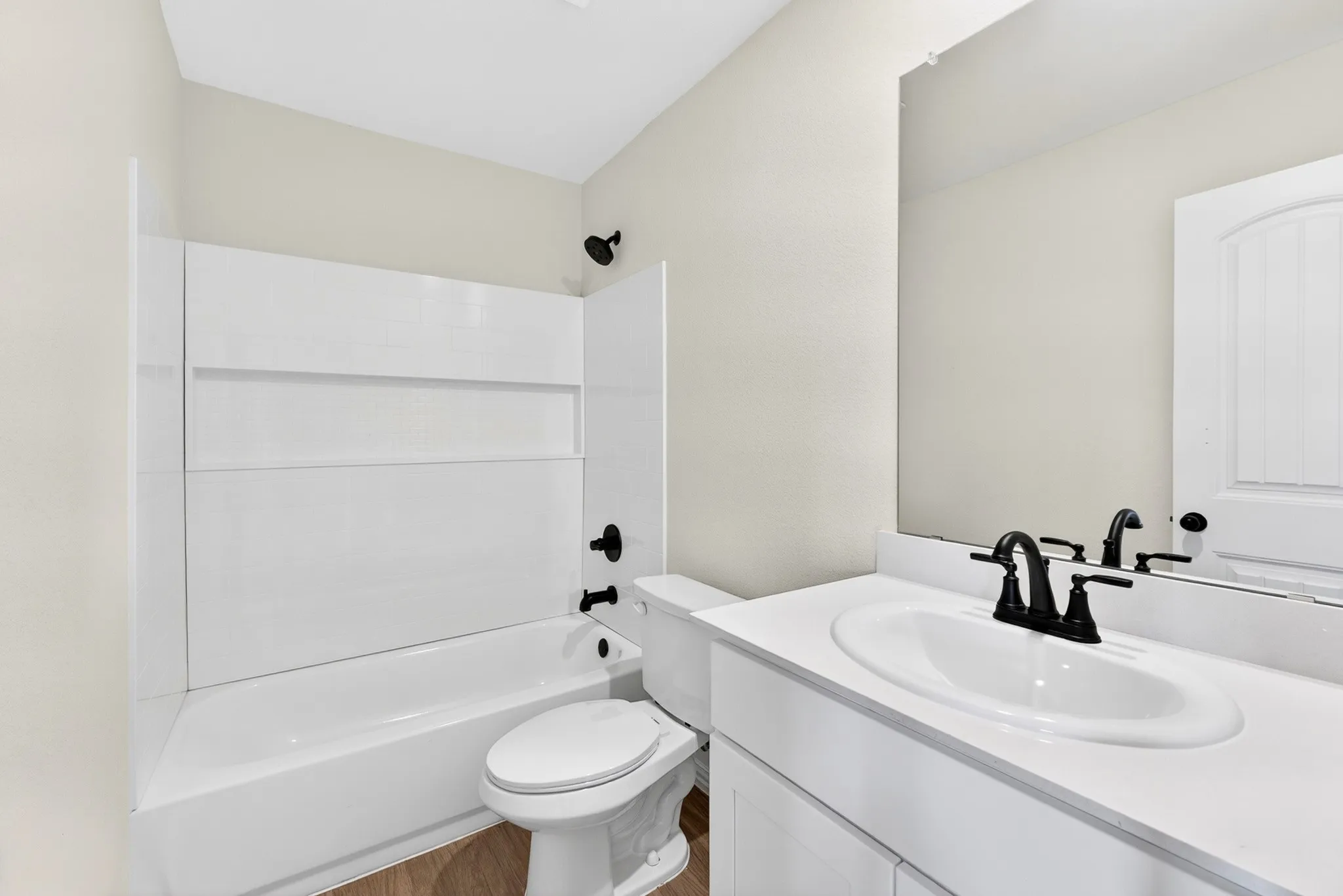 Bathroom featuring a white vanity with an integrated sink, matte black fixtures, a built-in tub with a shower, and wood-finish flooring