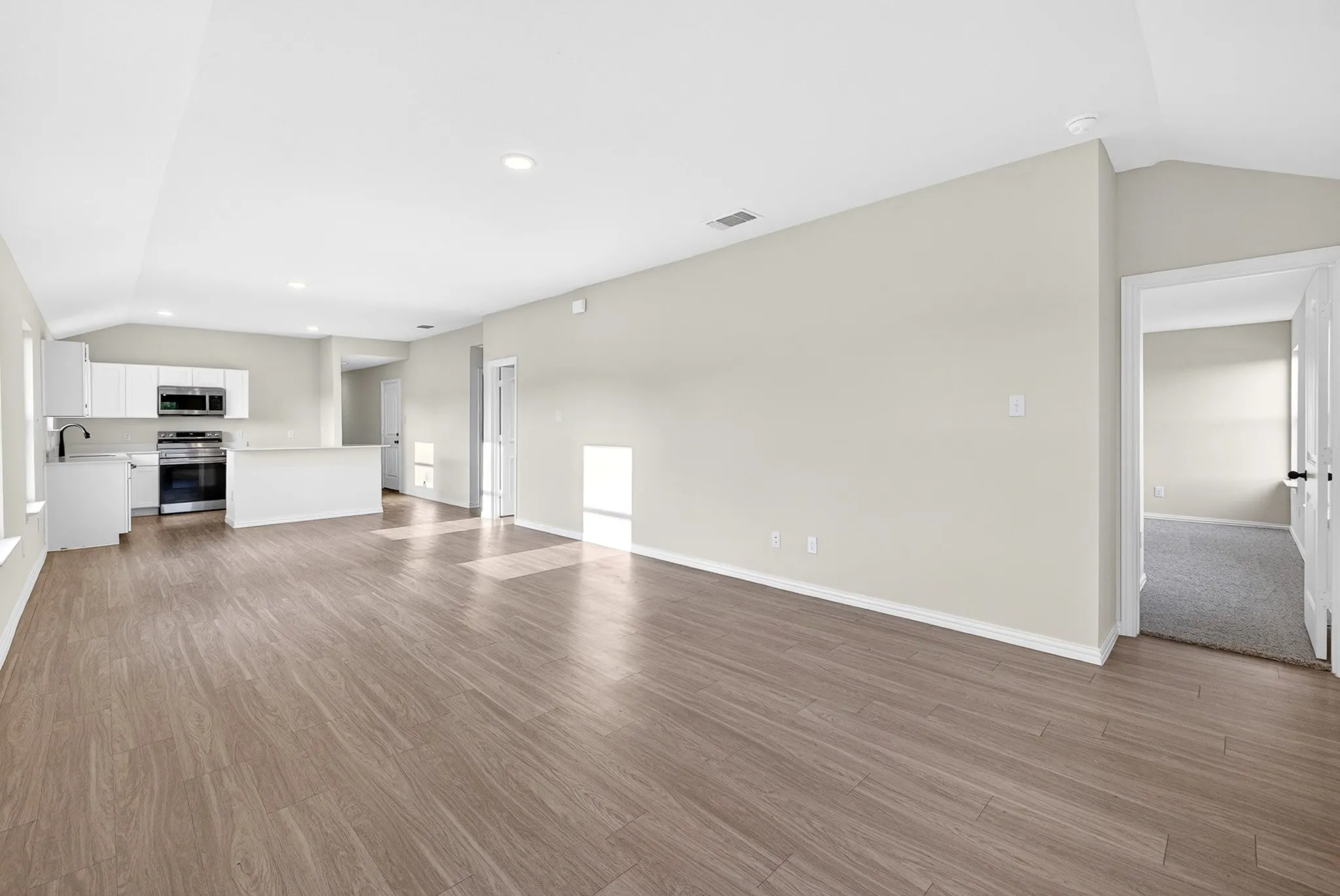 Open-concept living area showcasing wood-finish flooring throughout, recessed ceiling lighting, and a bright, neutral color palette