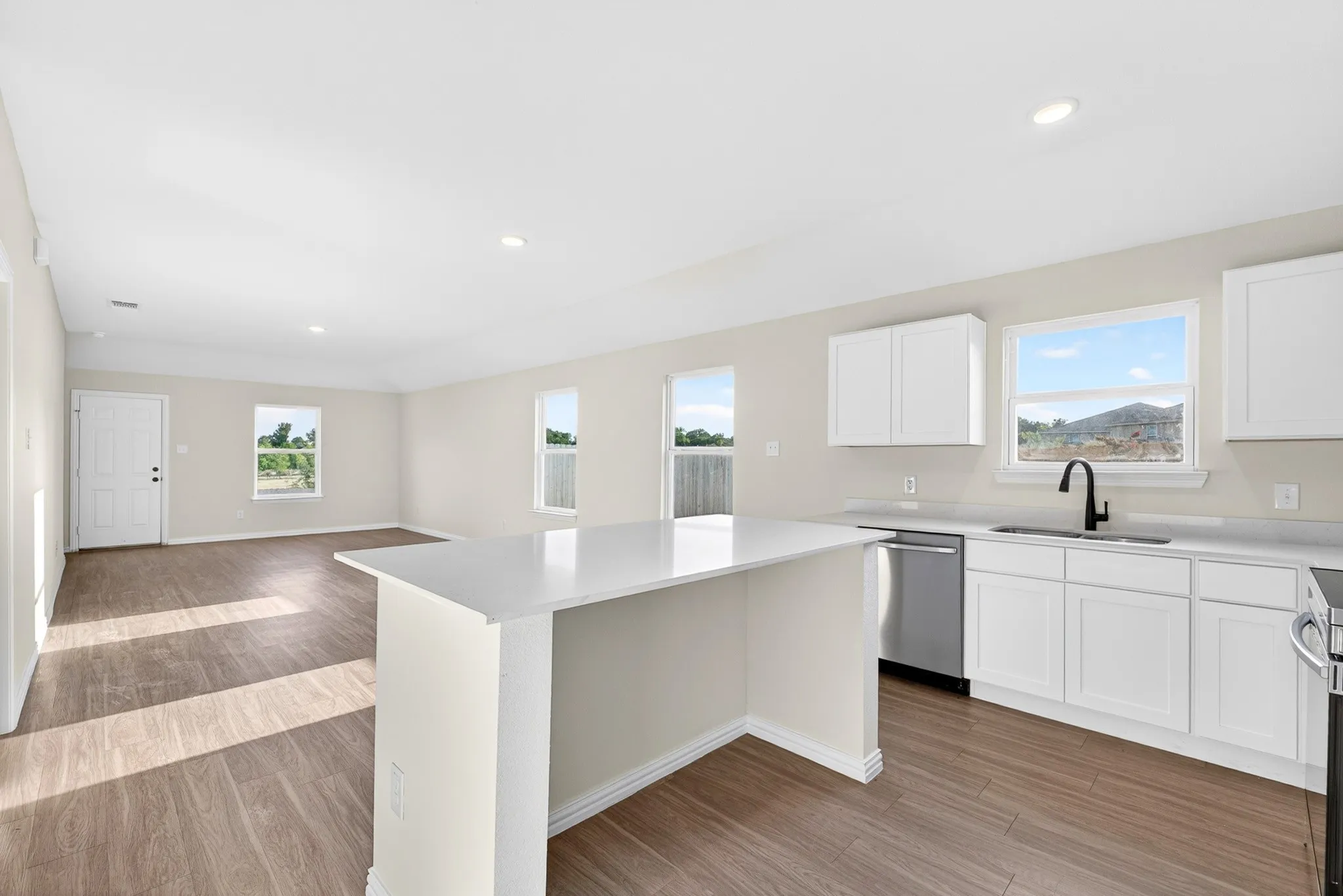 Open-concept kitchen and living area featuring white cabinetry, stainless steel appliances, a large island with waterfall-edge countertop, wood-finish flooring throughout, and abundant natural light from multiple windows with mountain vistas
