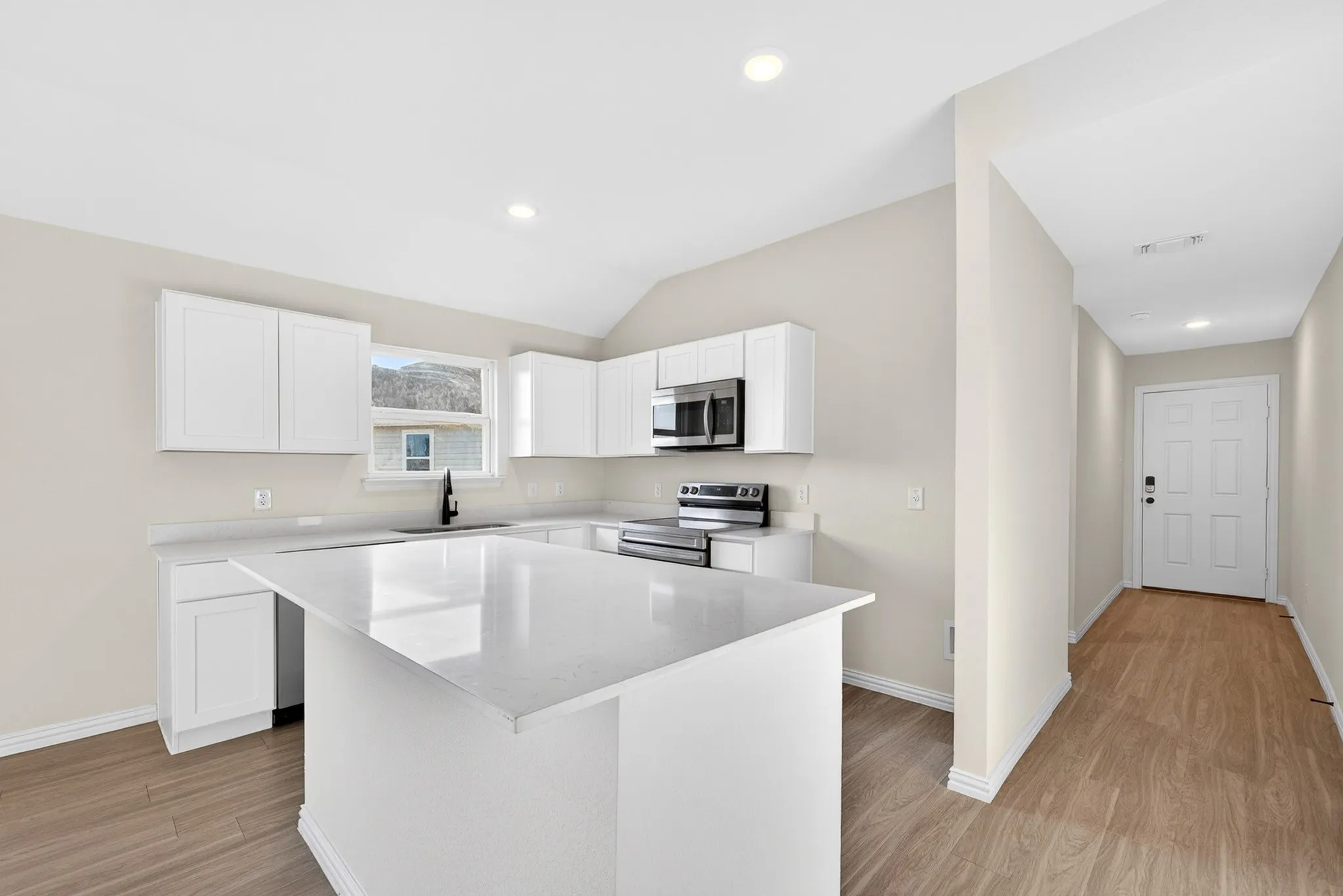 Kitchen featuring white cabinetry, light-toned countertops, stainless steel appliances, and wood-finish flooring