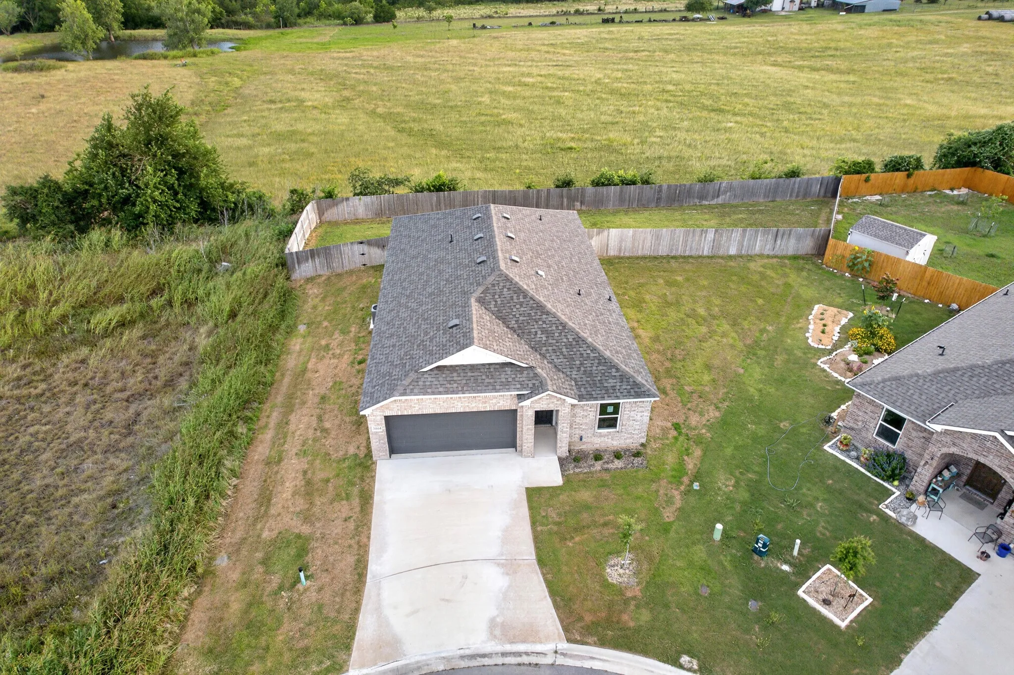 Brick exterior with an attached garage, paved driveway, and fenced backyard with a storage shed