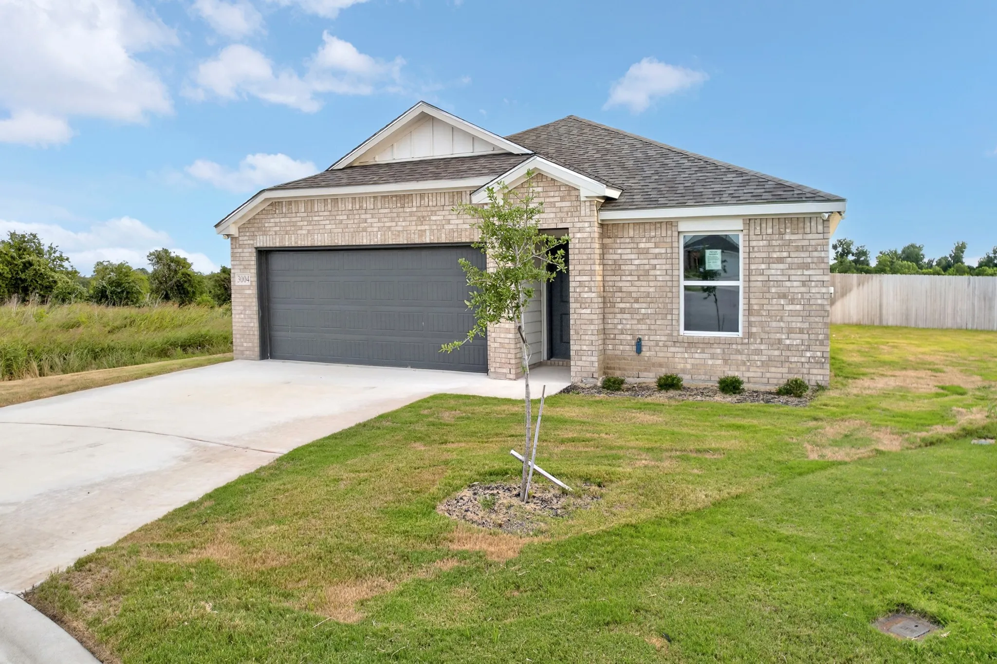 Brick exterior with a dark gray garage door, a concrete driveway, and a partially fenced yard