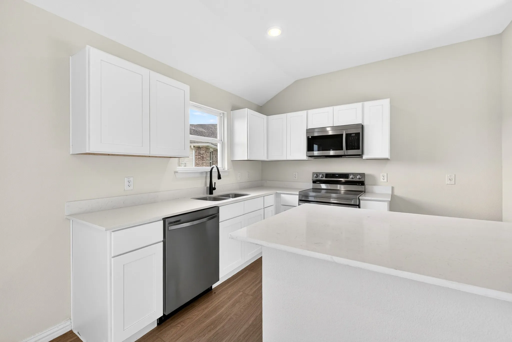 White shaker-style cabinetry, stainless steel appliances, wood-finish flooring, white countertops, and a kitchen island