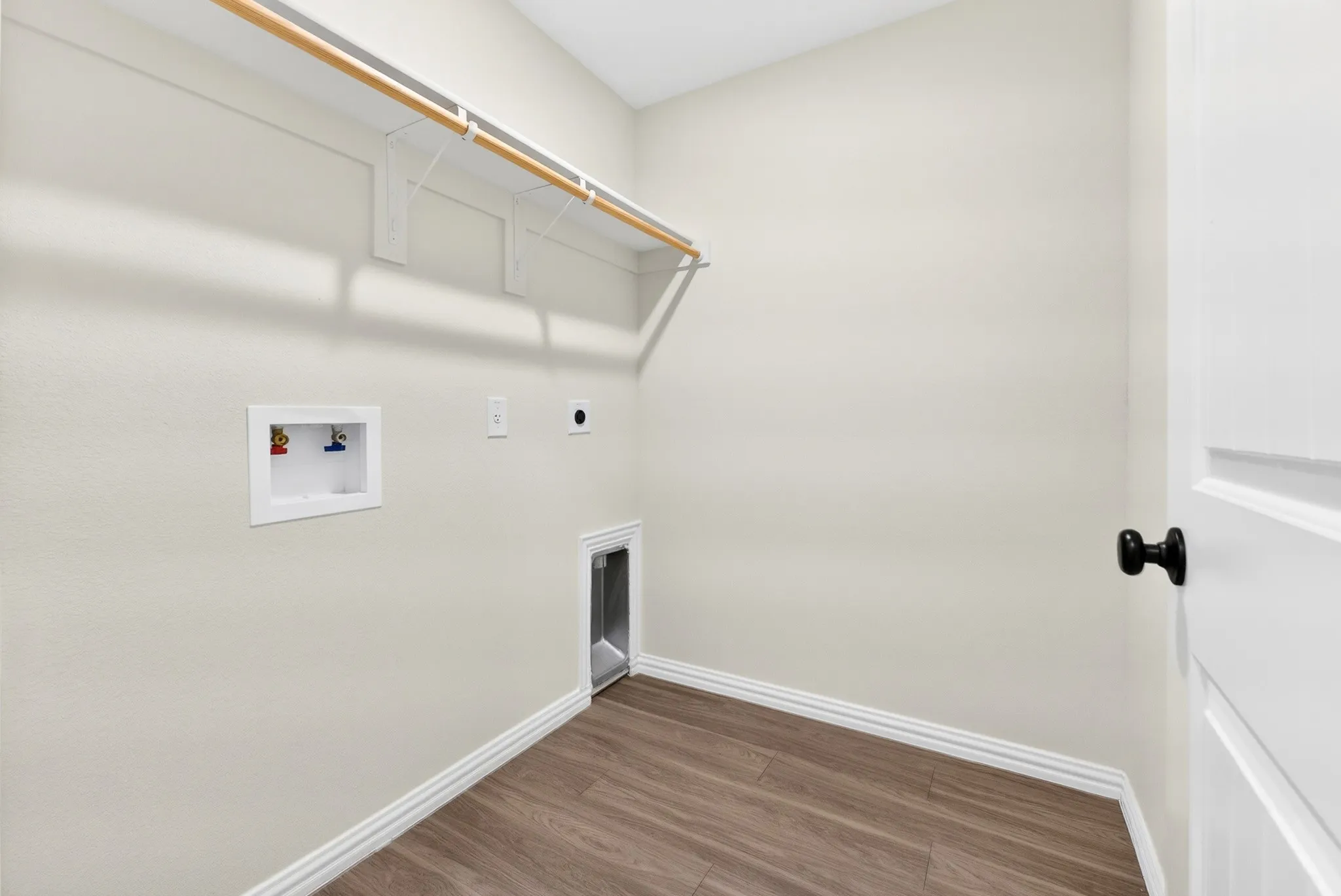 Utility room featuring wood-finish flooring, light-toned walls, a built-in hanging rod with shelving, and appliance hookups